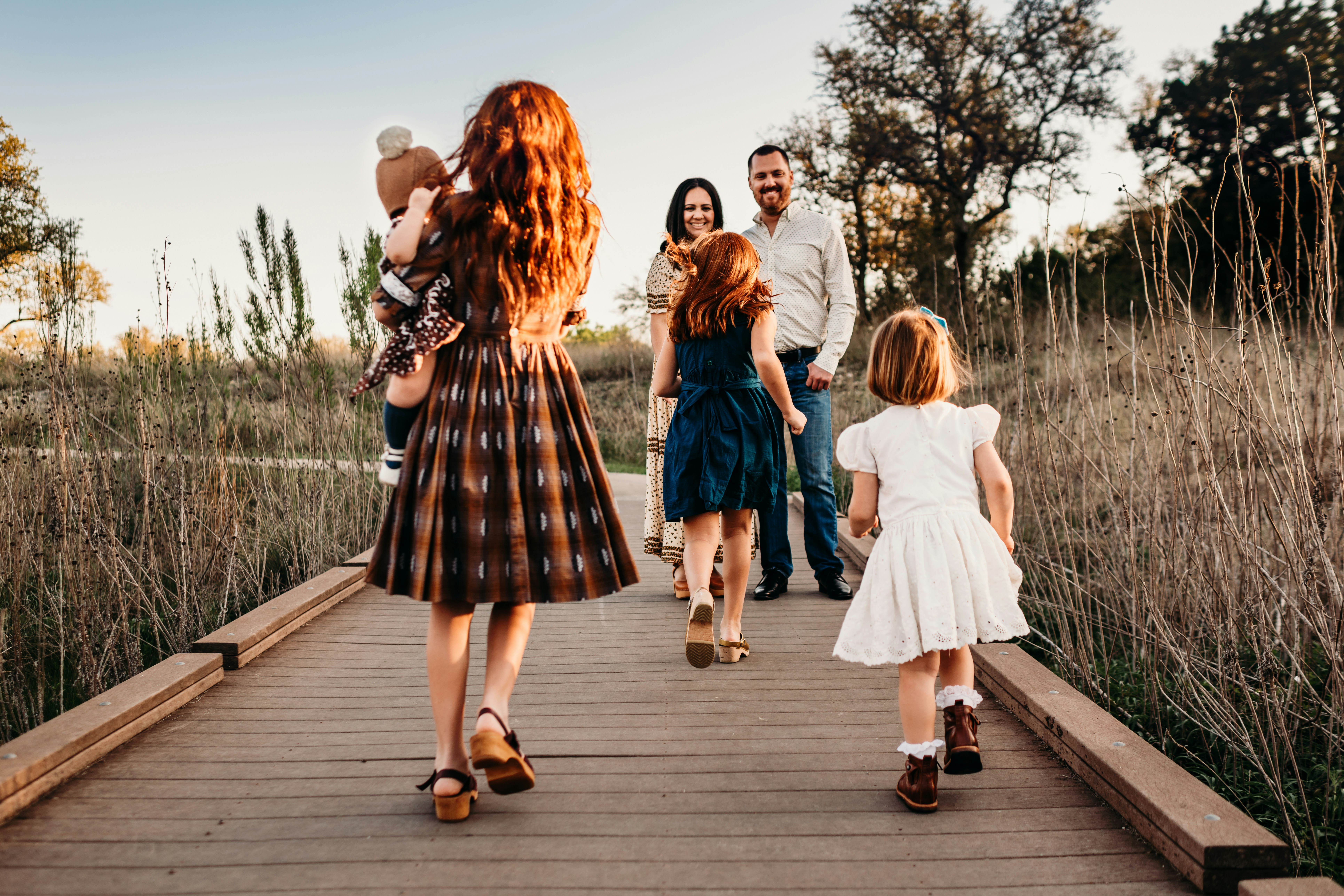 Family walking on a wooden path in a grassy field during sunset