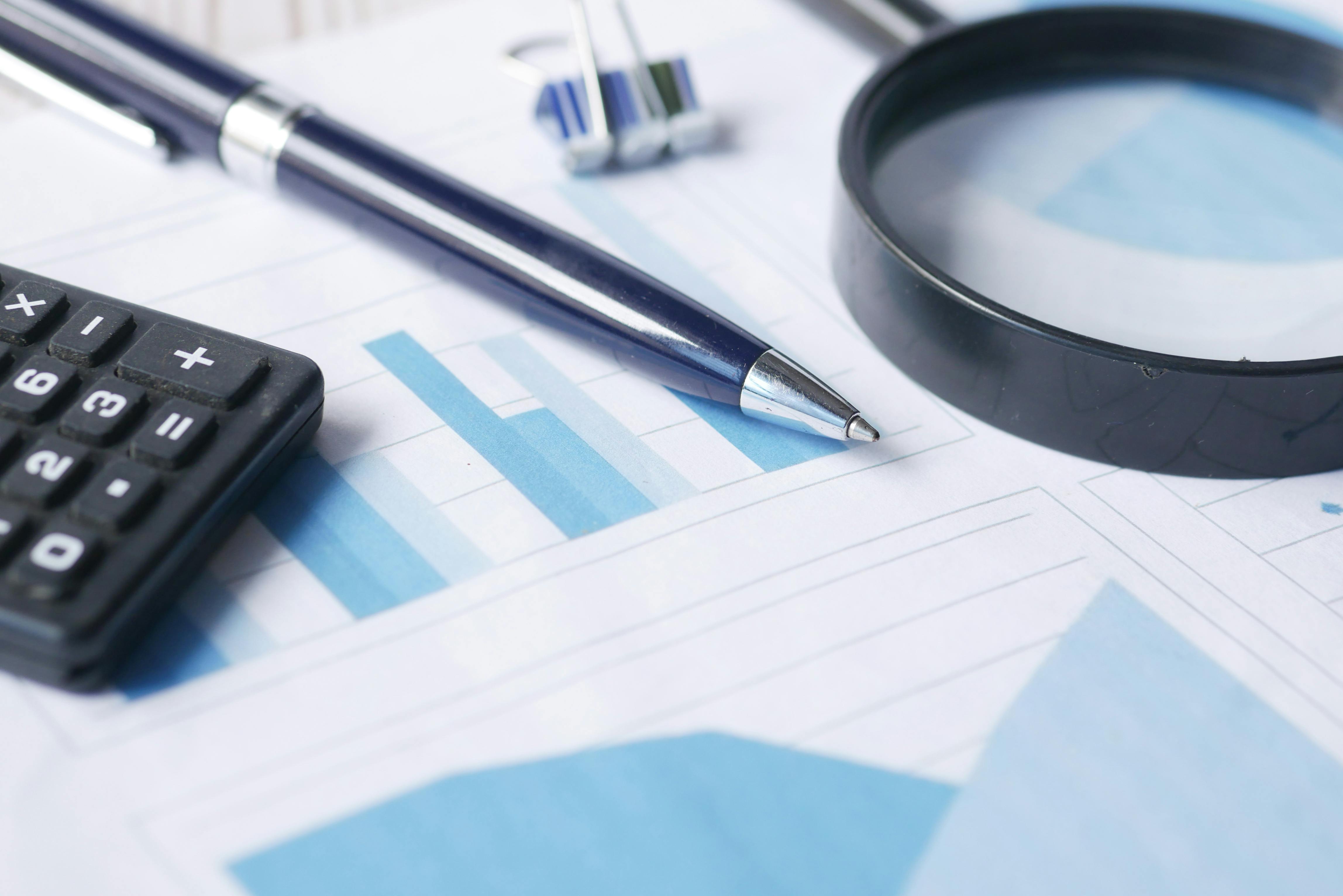 Calculator, pen, magnifying glass, and charts on a desk