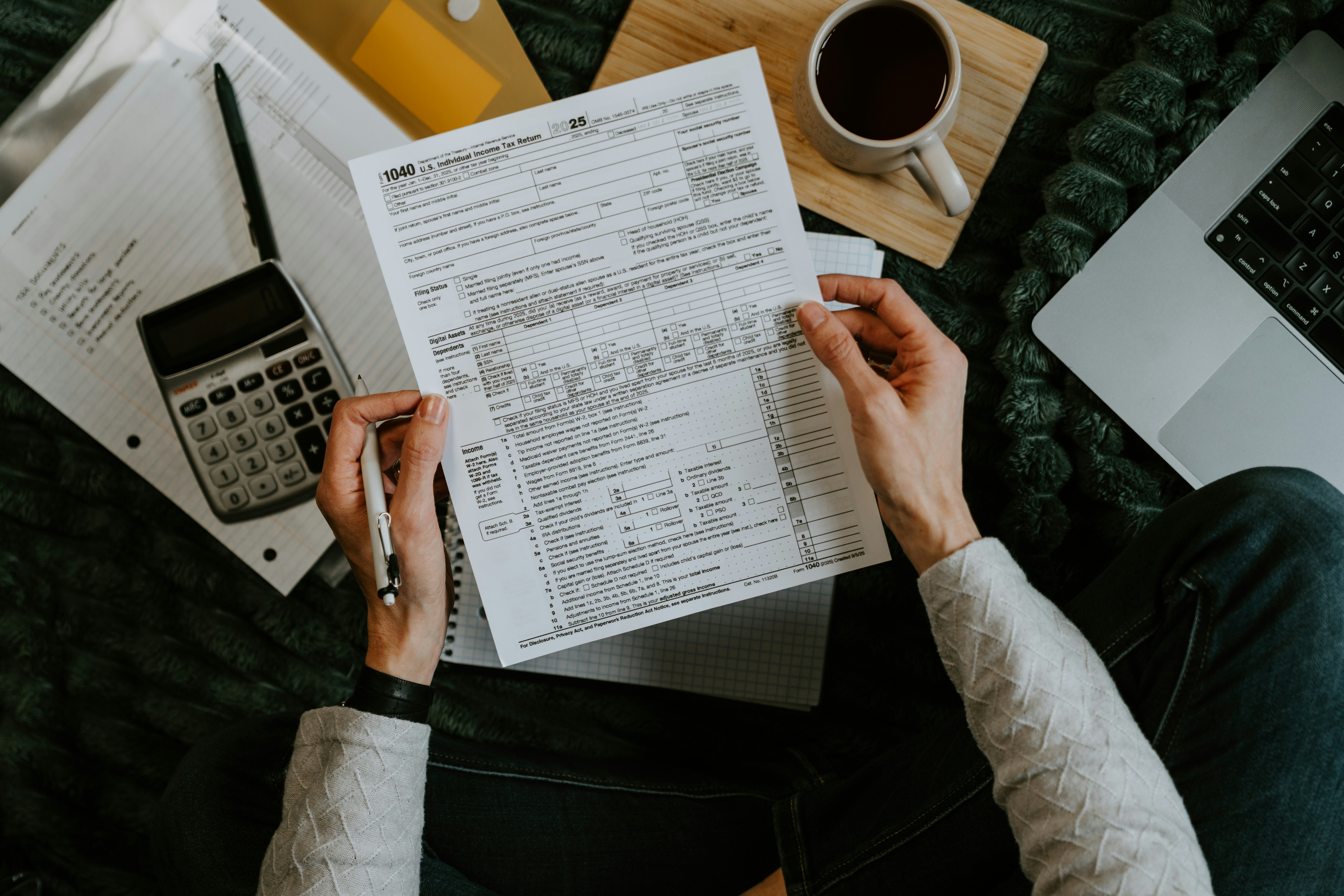 Person holding a tax form with a calculator and laptop nearby
