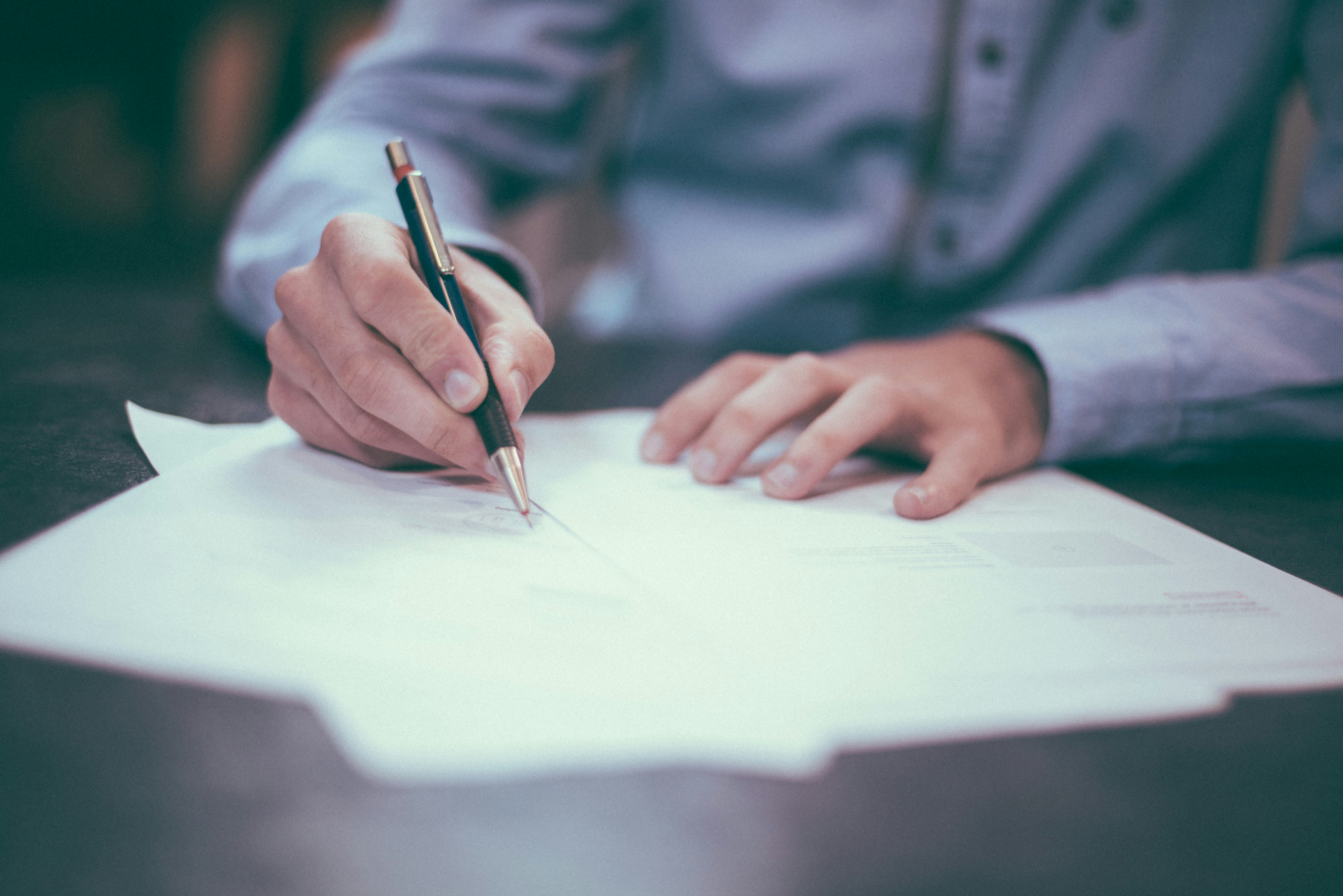 Person writing on paper with a pen at a desk