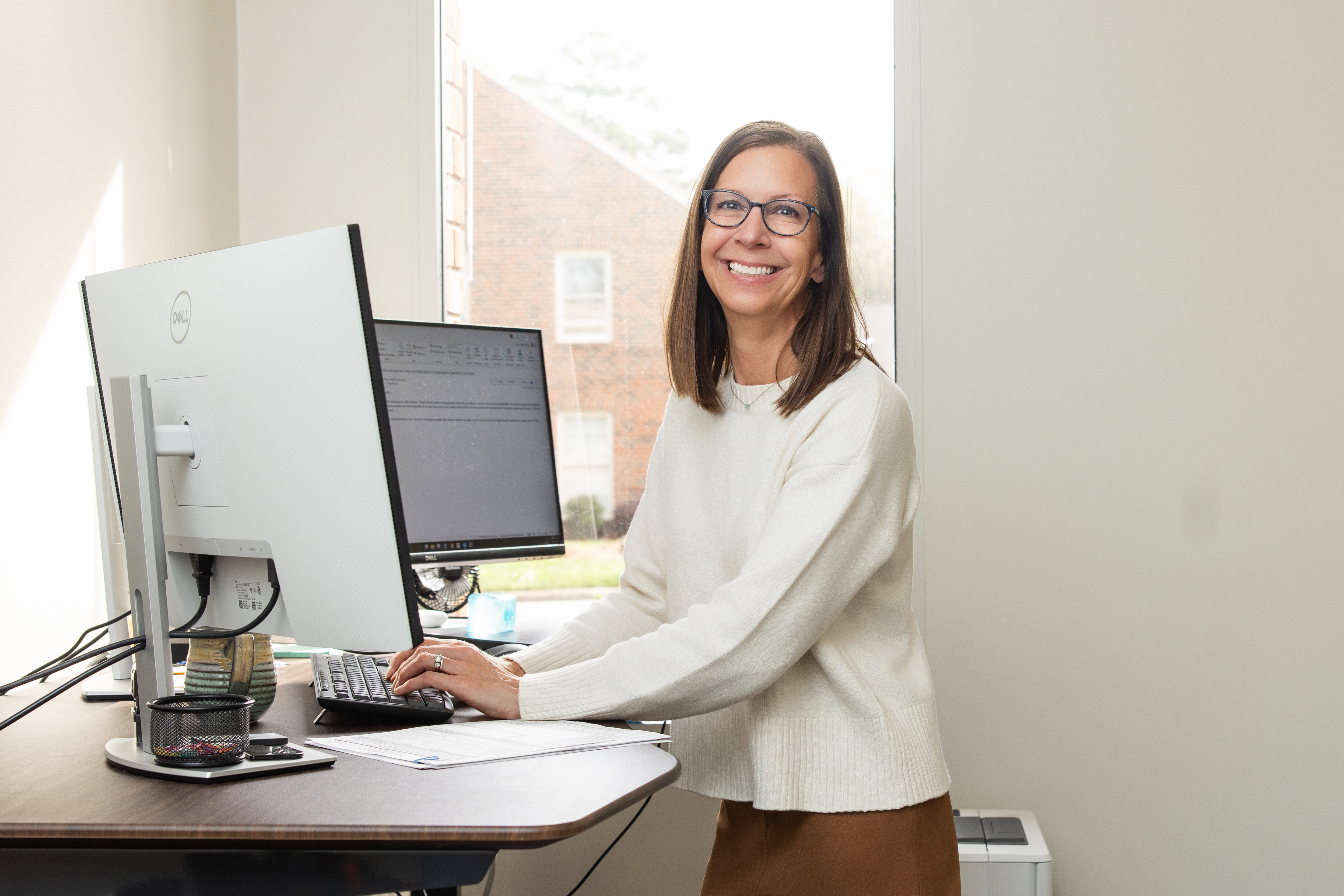 Smiling woman working at a standing desk with a computer in an office.