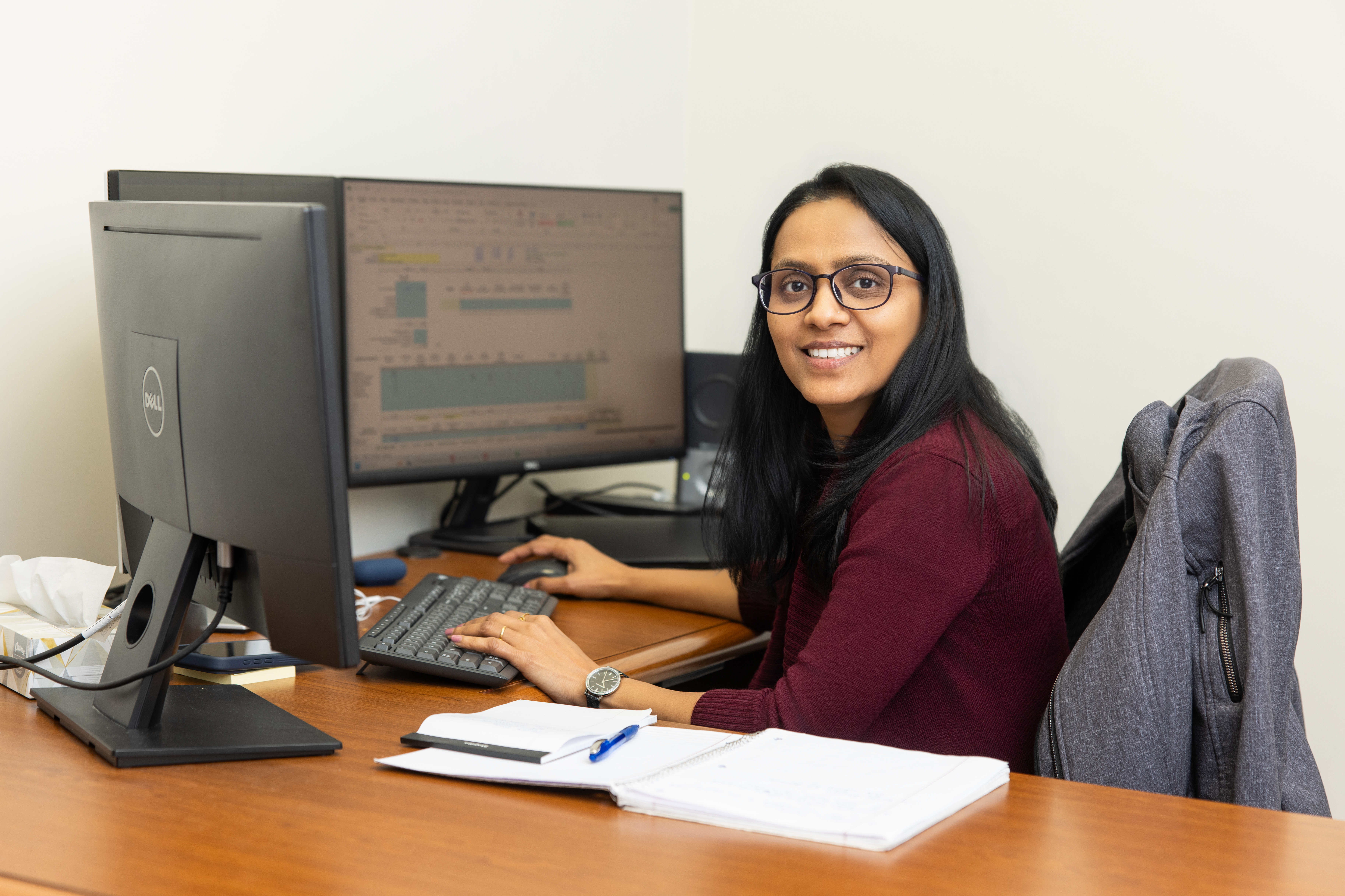 Woman working at a desk with dual monitors and taking notes.