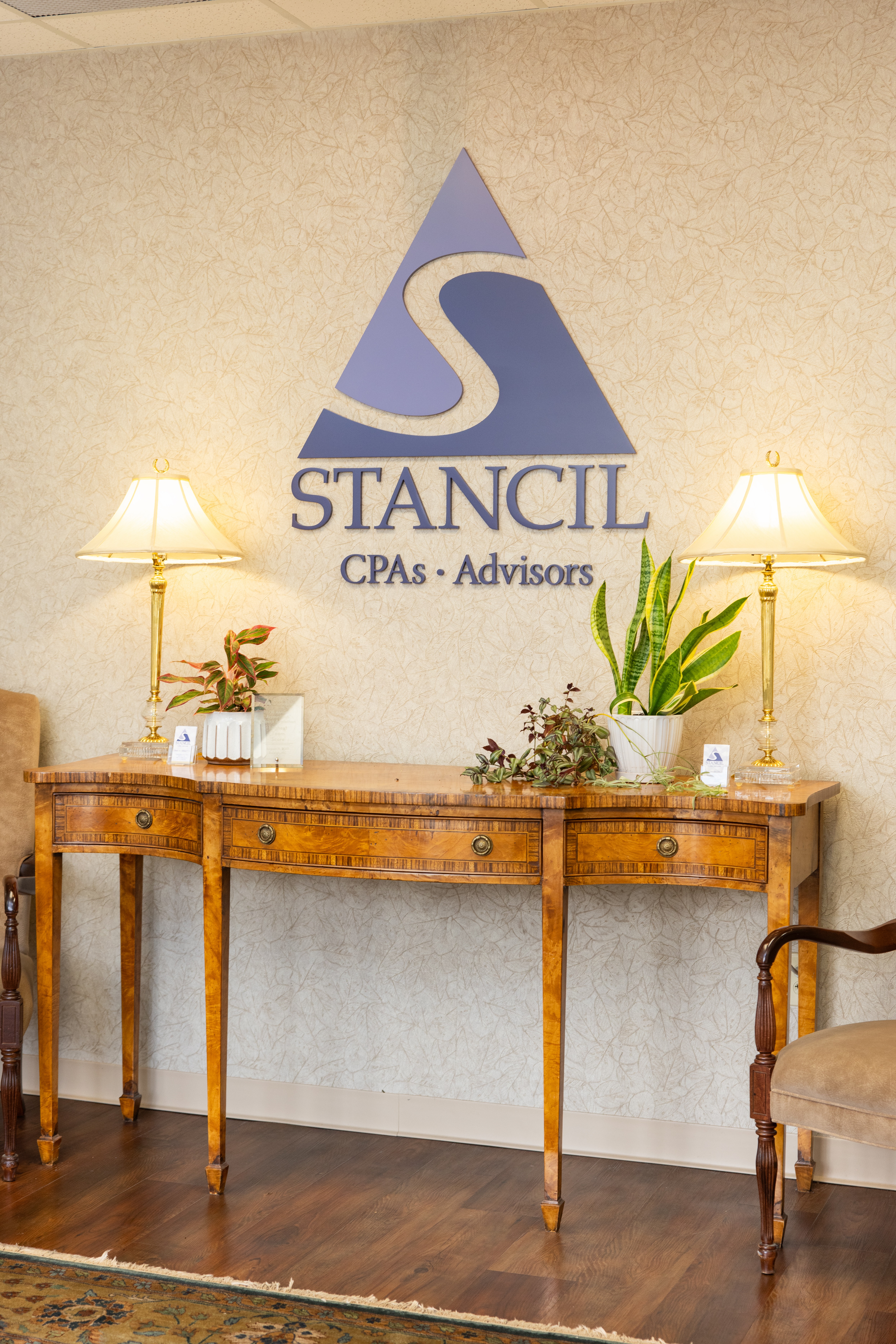 Reception area with a wooden table, lamps, and plants under a CPA firm logo.