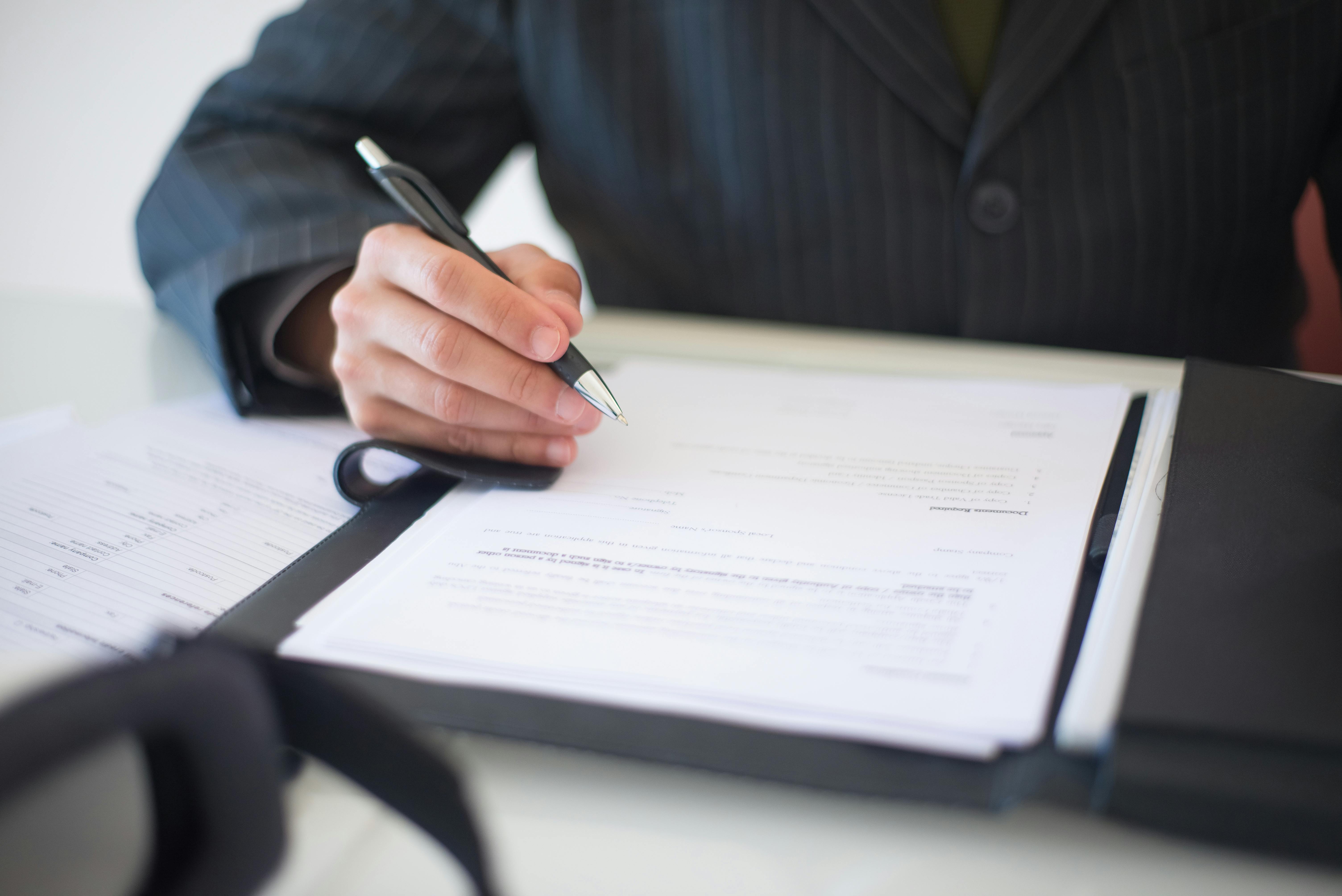 Person in a suit reviewing and signing documents at a desk