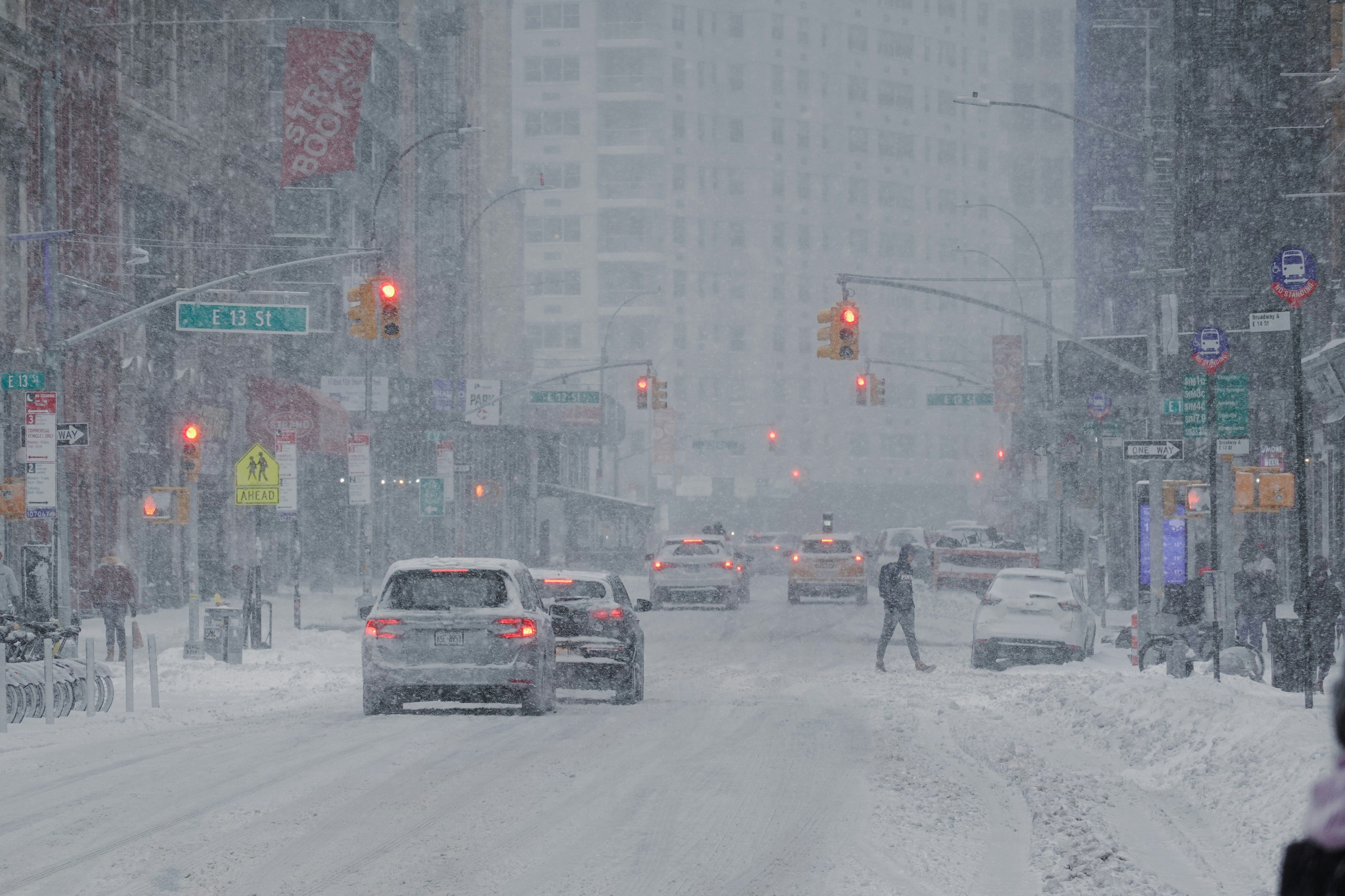City street covered in snow with cars and pedestrians during a snowstorm