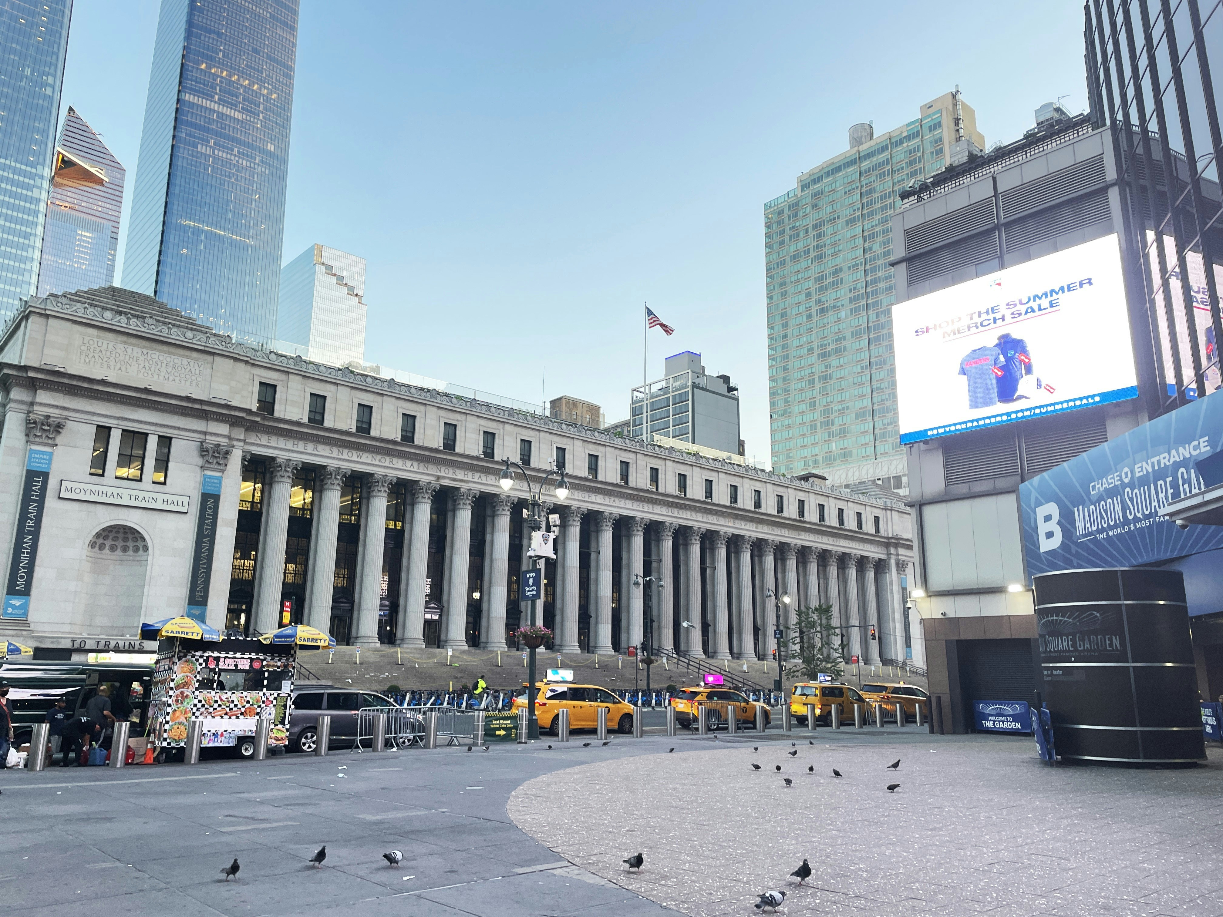 Street view of a historic building with columns, surrounded by skyscrapers and taxis.