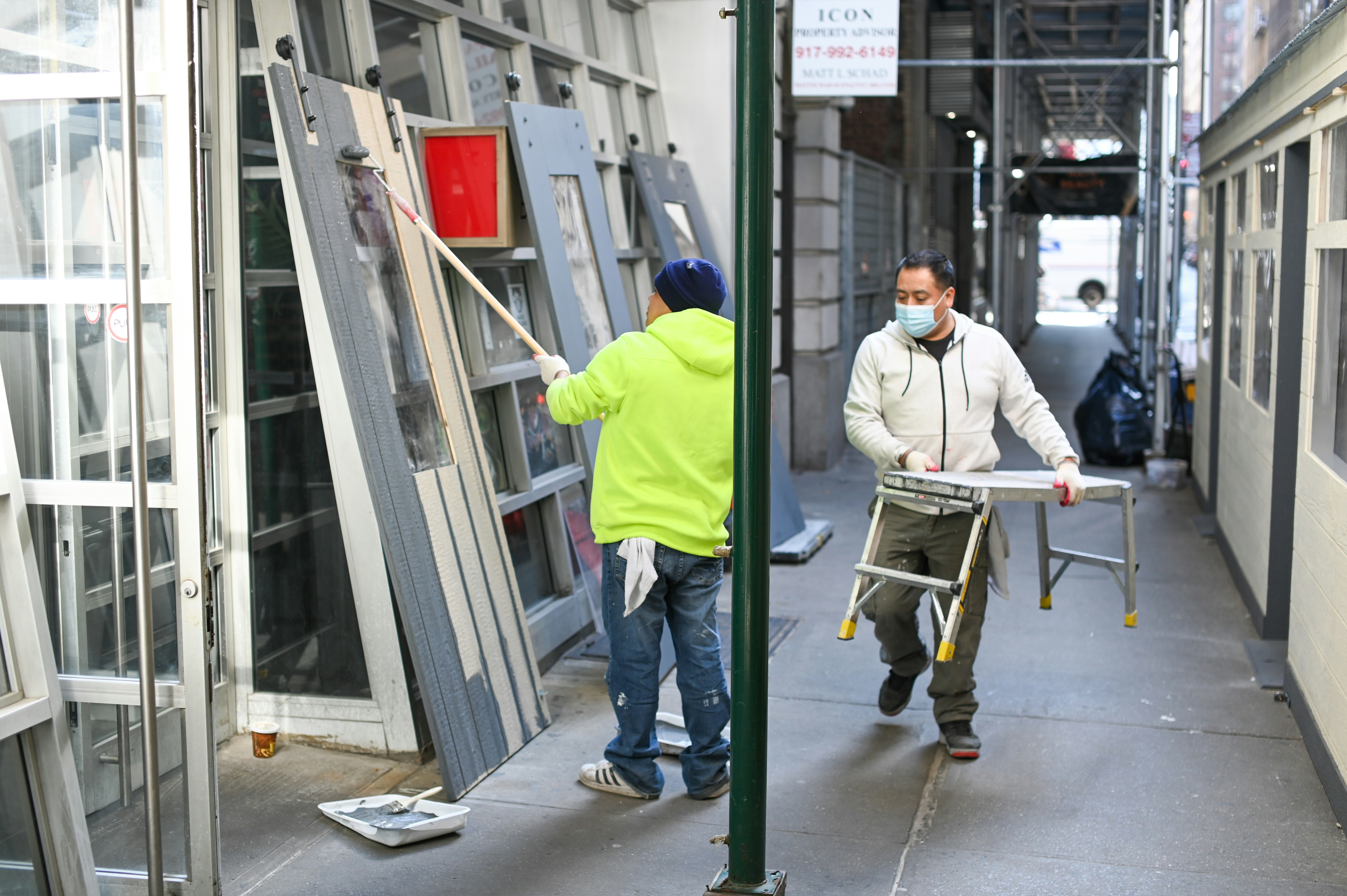 Workers painting and carrying a ladder on a city sidewalk