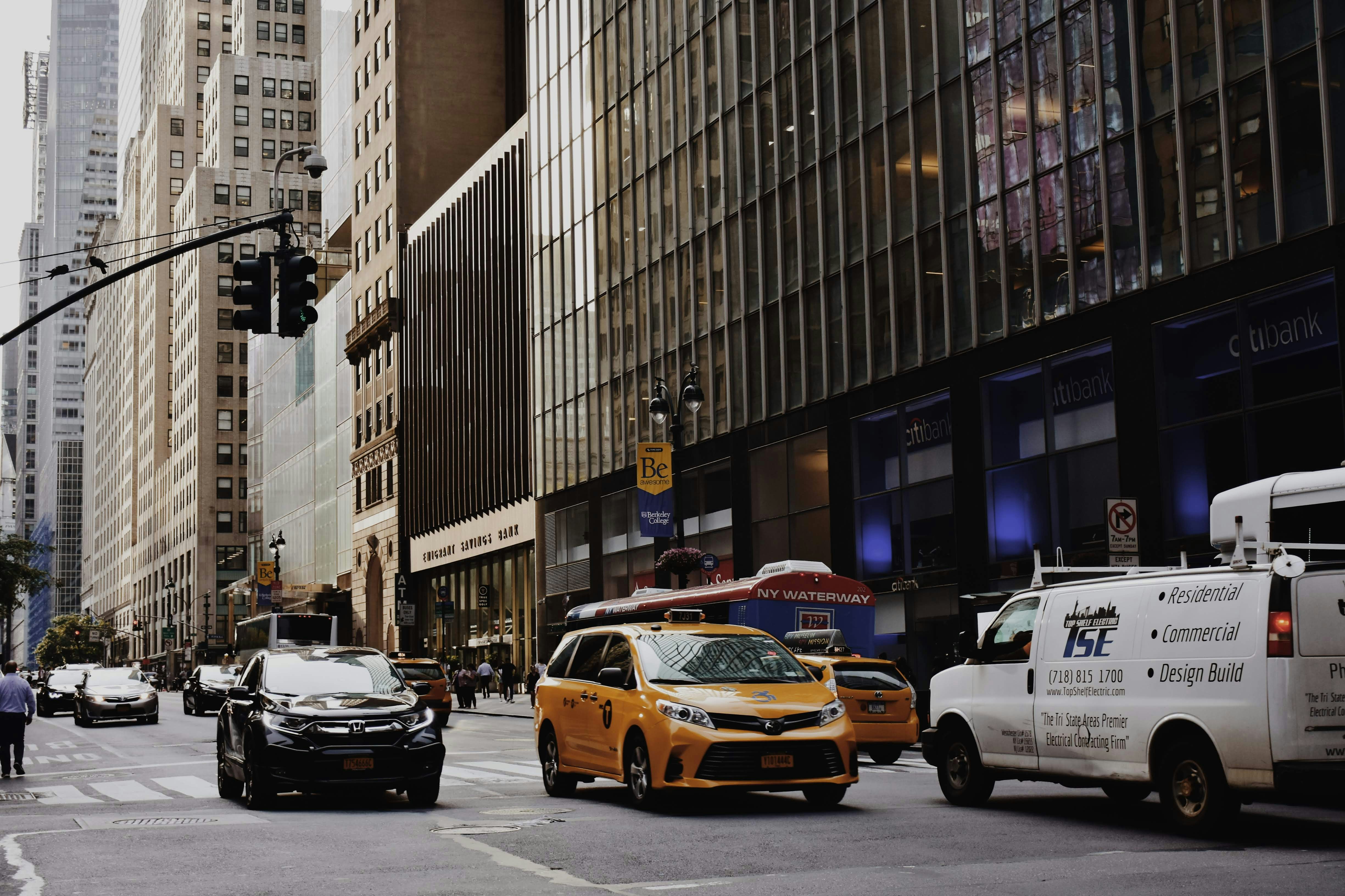 Busy city street with cars, including a yellow taxi, and tall buildings
