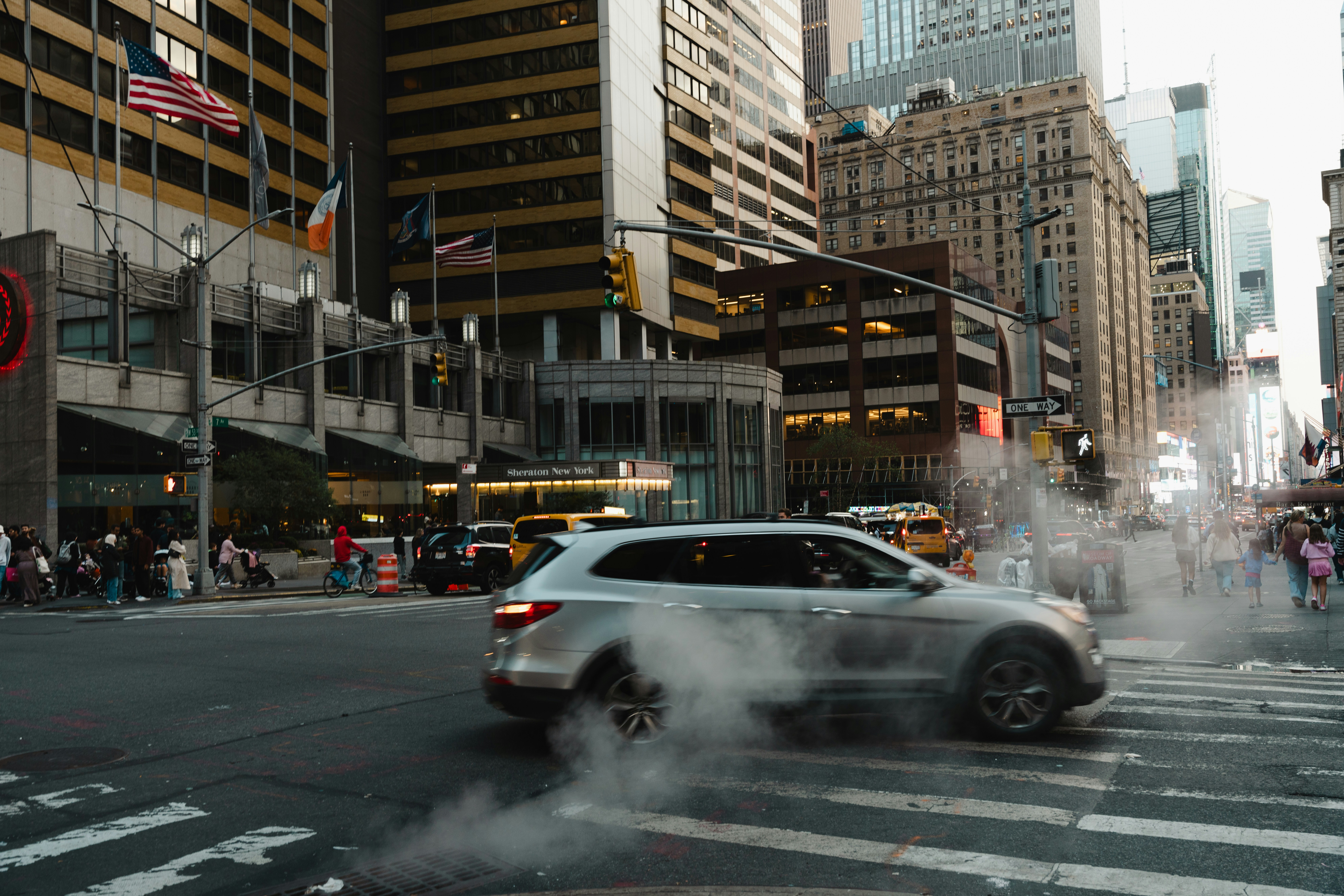 Busy city street with cars, buildings, and steam rising from a manhole