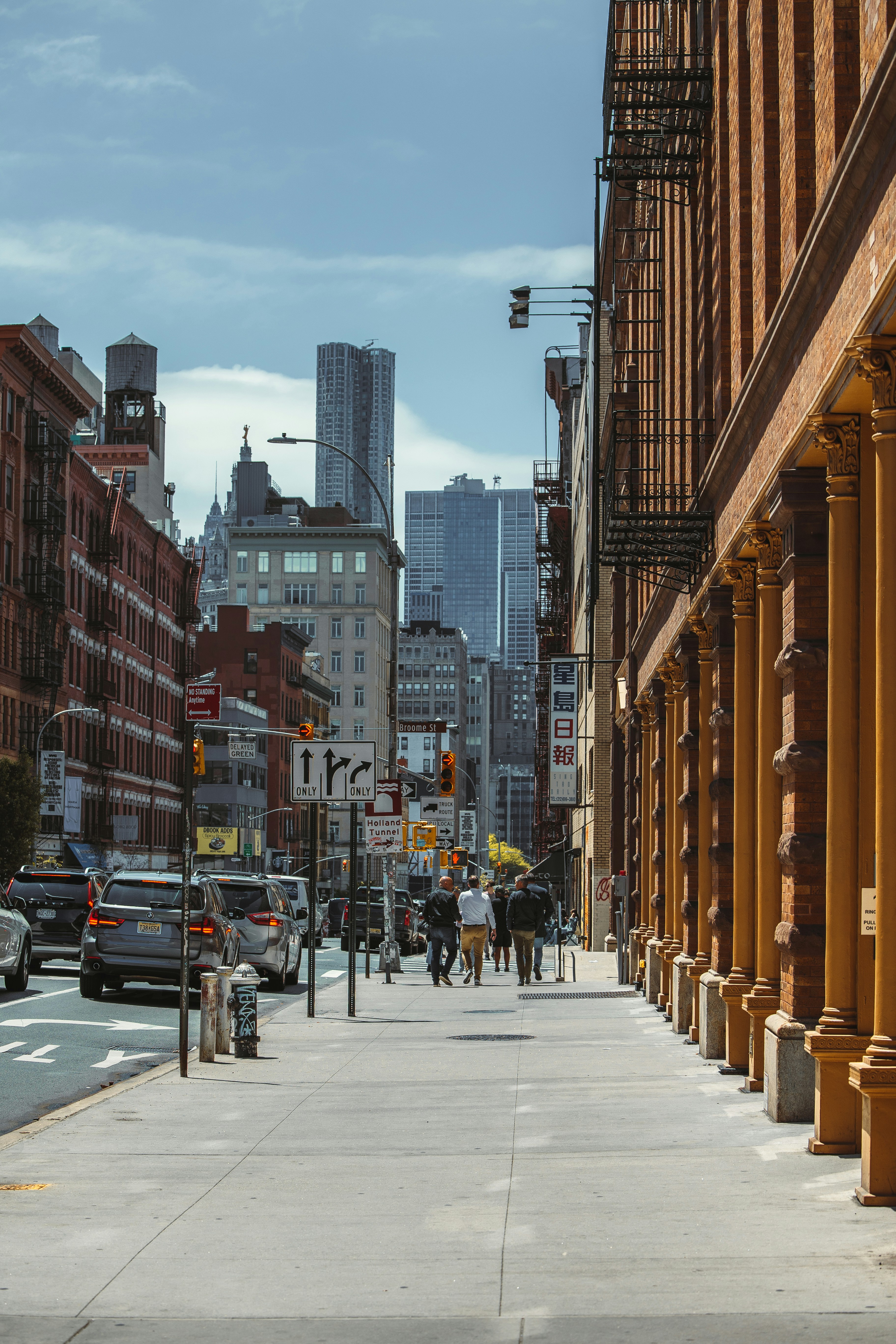 Urban street scene with people walking and cars parked, tall buildings in the background