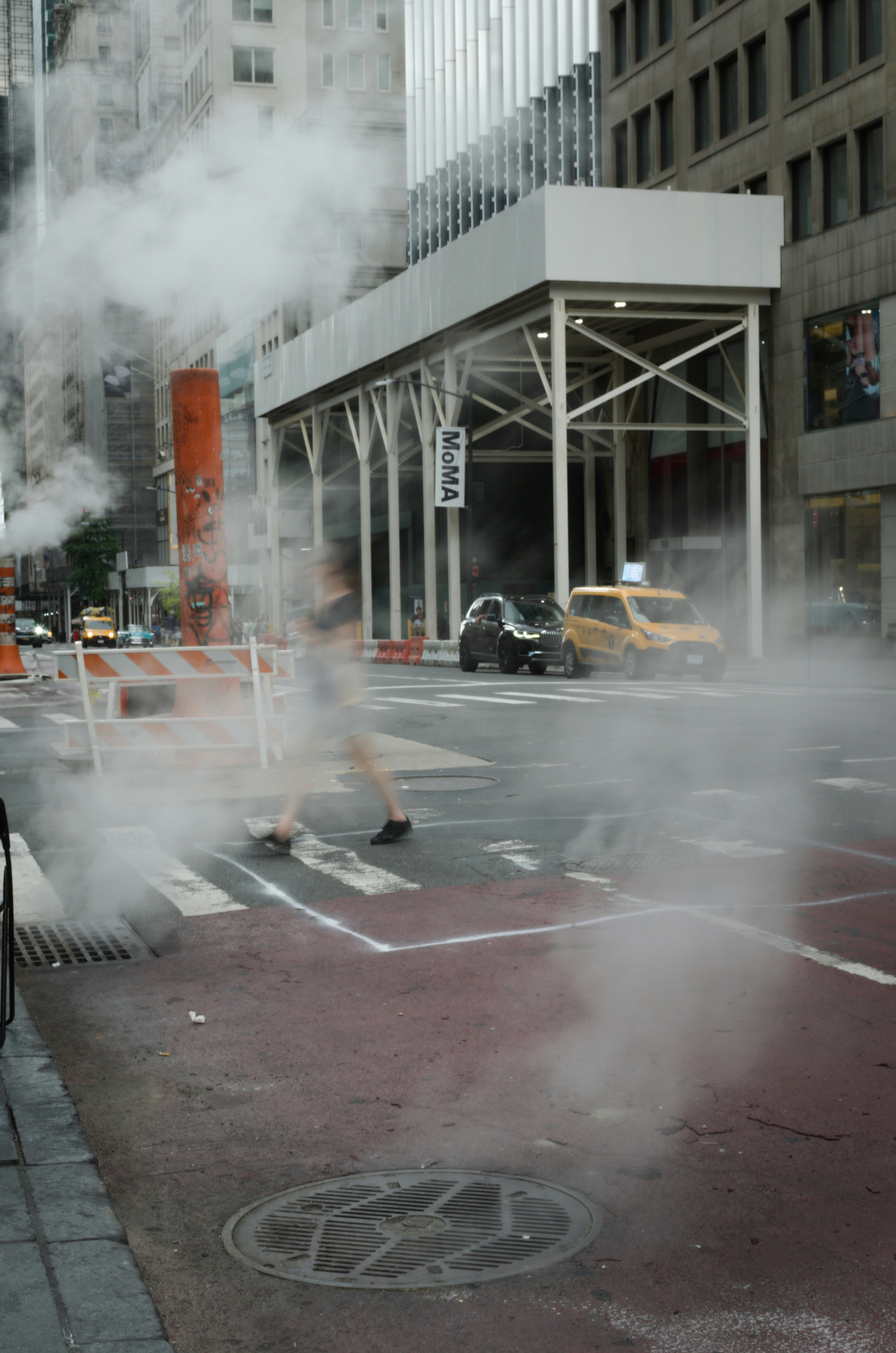Urban street scene with steam rising and a blurred pedestrian crossing