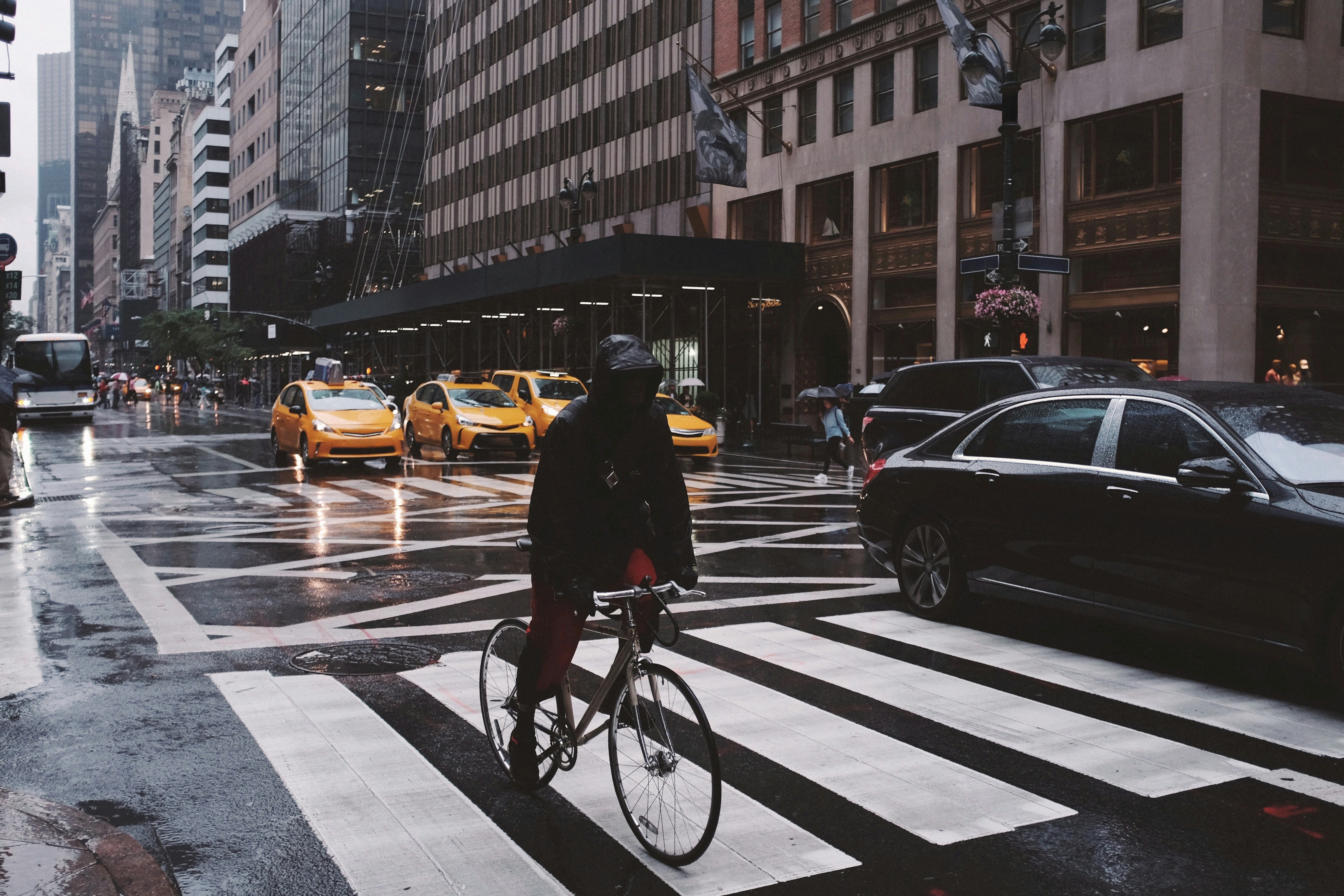 Cyclist crossing a busy city street with yellow taxis and tall buildings in the background