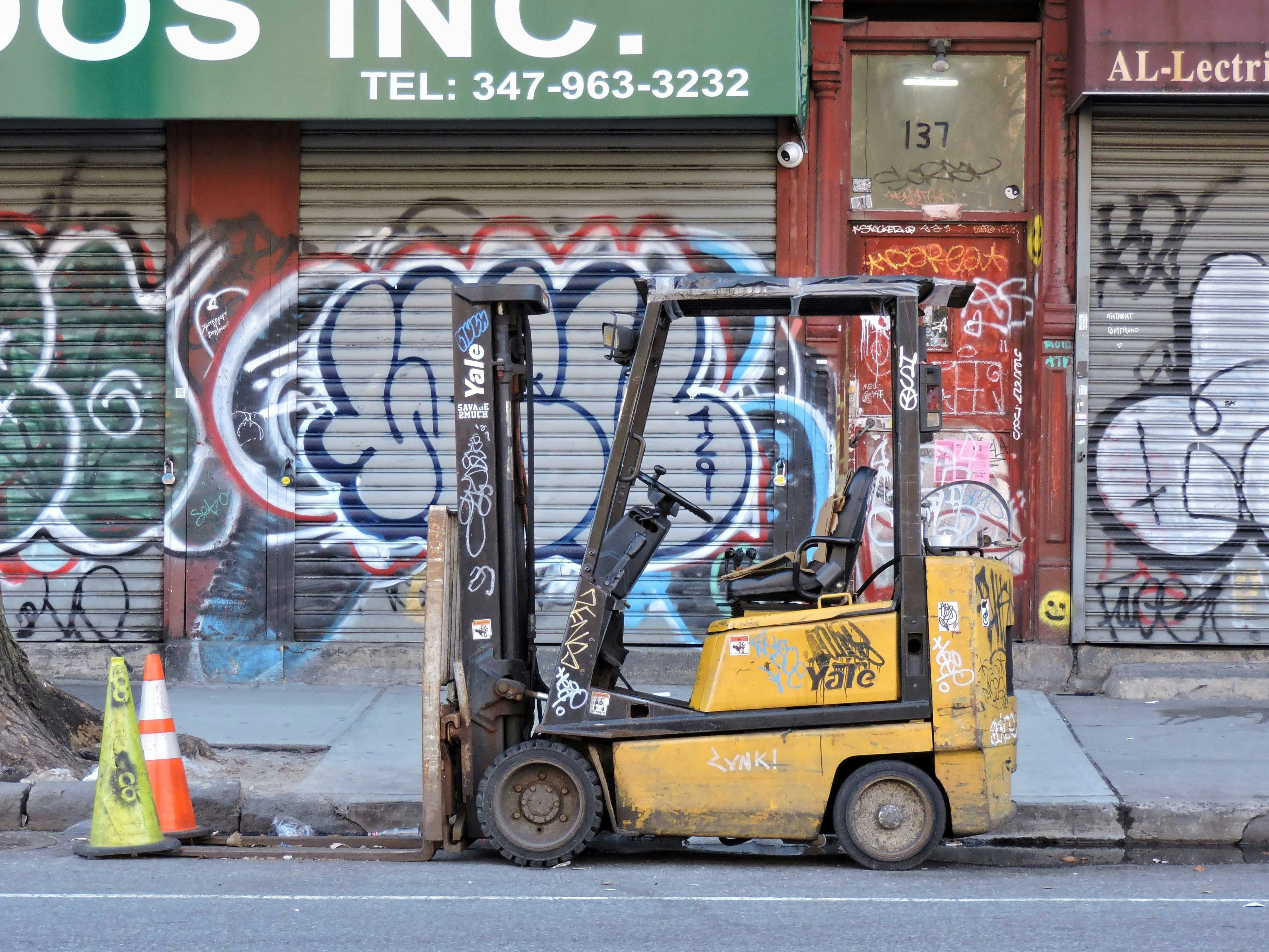 Forklift parked on a graffiti-covered urban street with traffic cones nearby