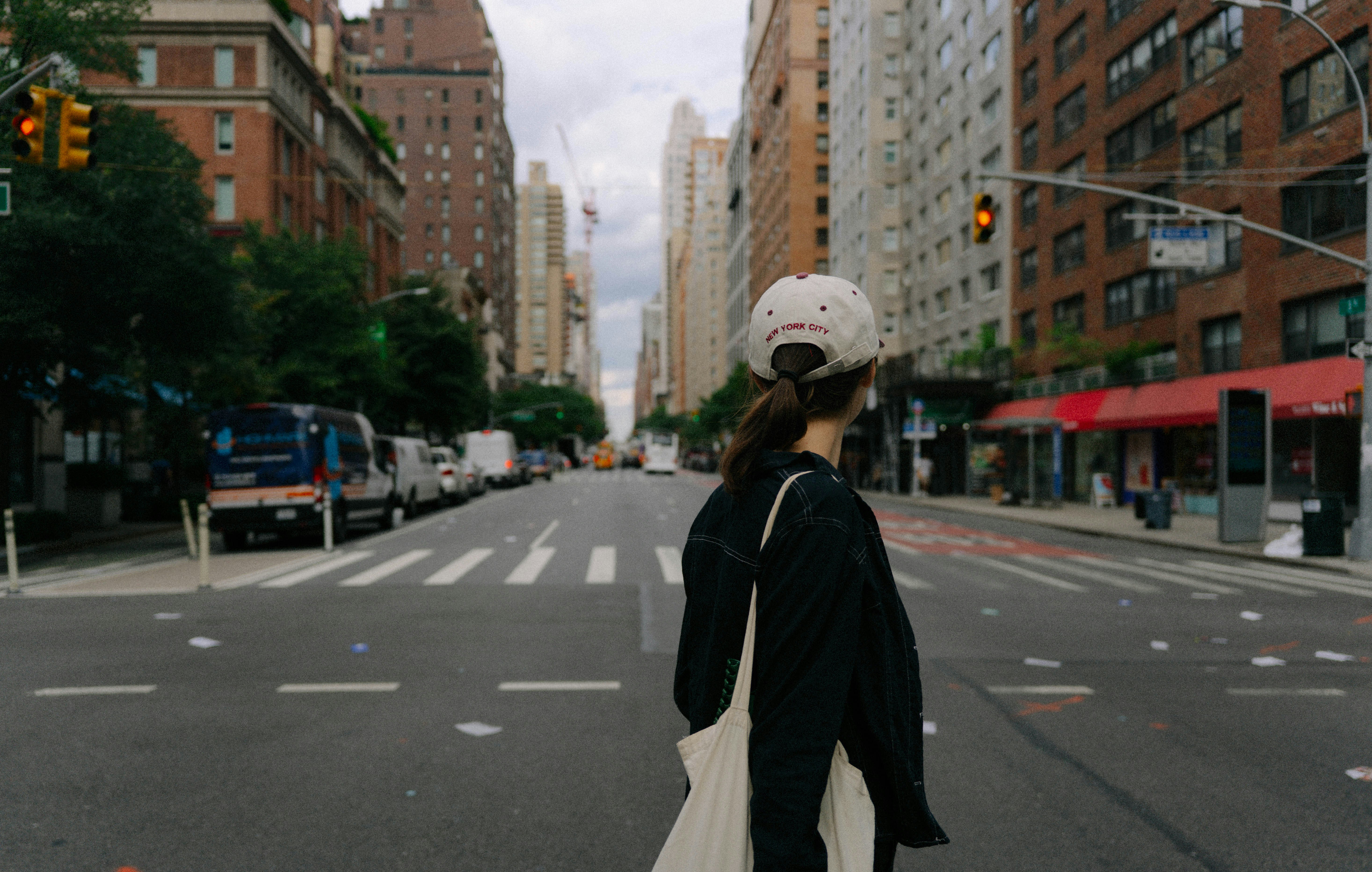 Person wearing a cap and carrying a tote bag standing on a city street
