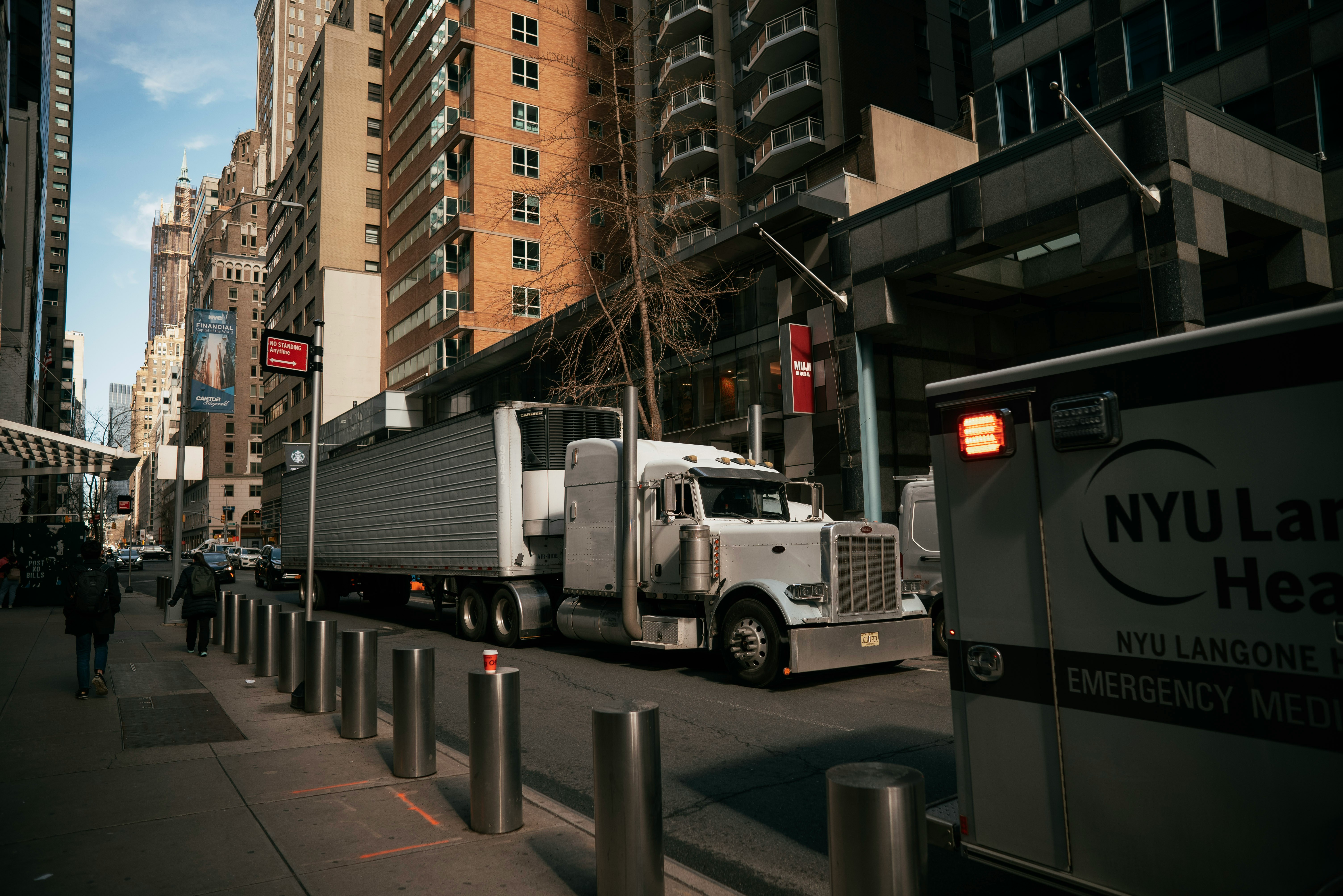A large truck and an ambulance on a busy city street with tall buildings.
