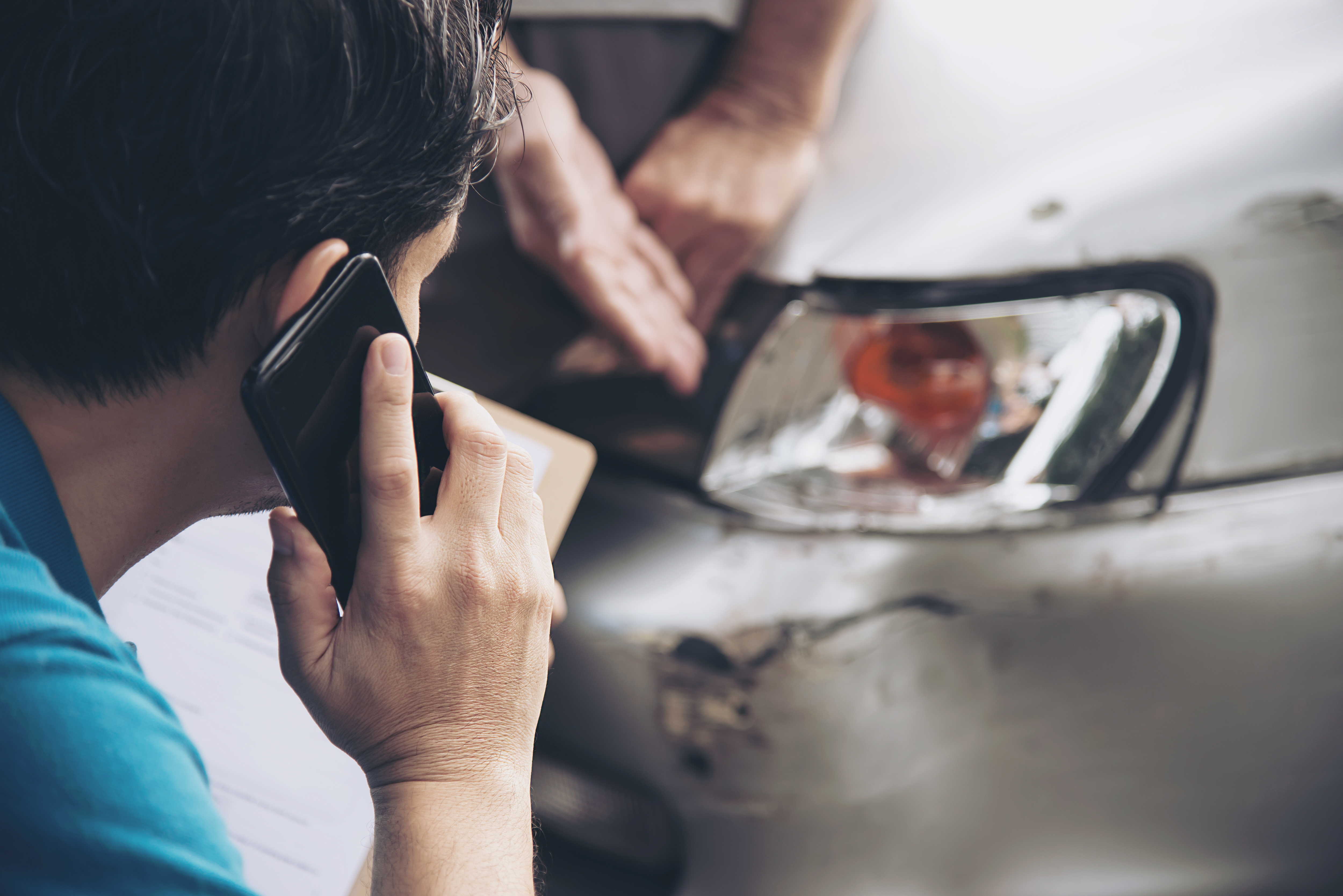 Person on phone inspecting car damage after an accident