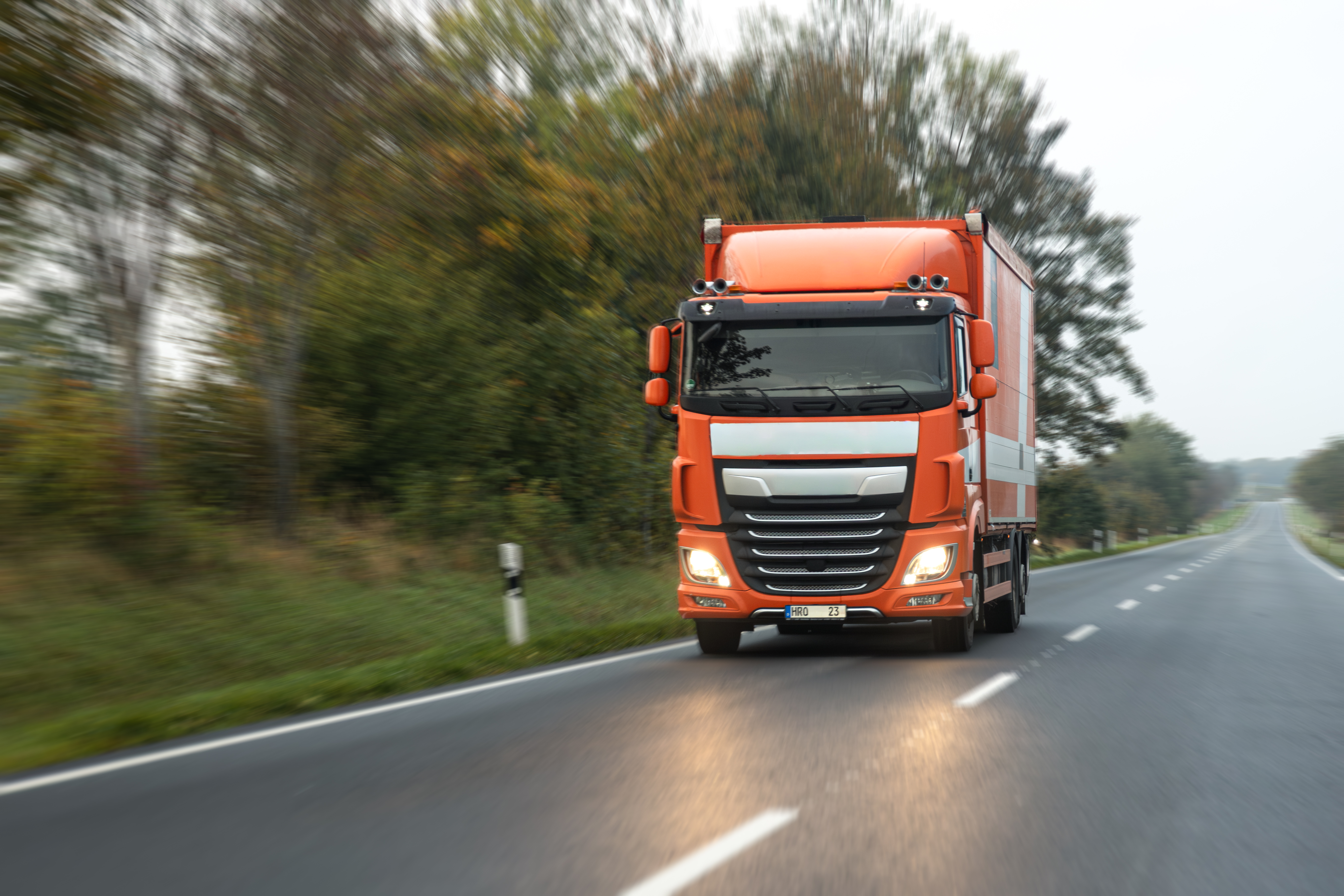 Orange truck driving on a rural road with trees in the background
