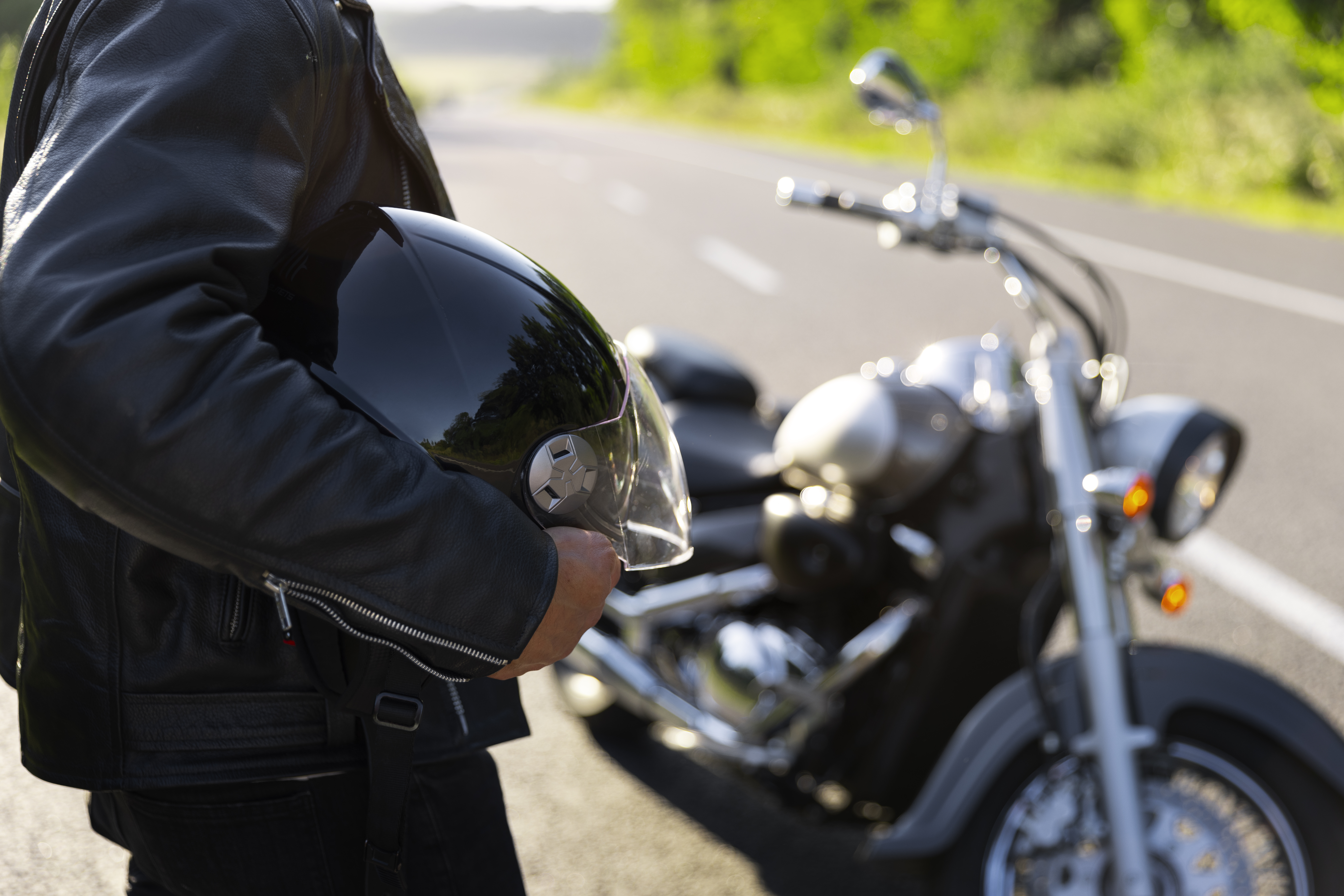Person holding a motorcycle helmet next to a parked motorcycle on a road
