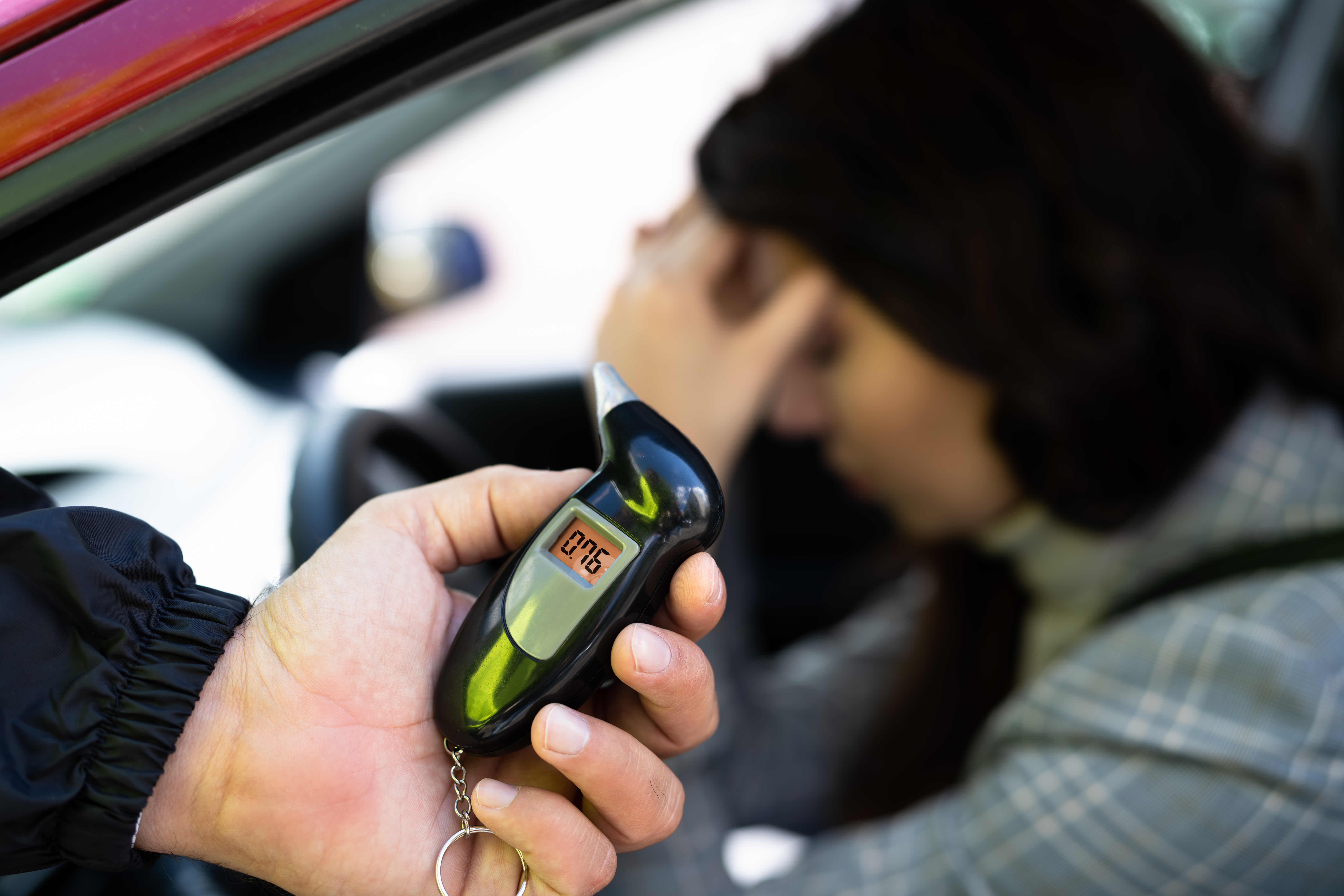 Person holding a breathalyzer near a distressed woman in a car