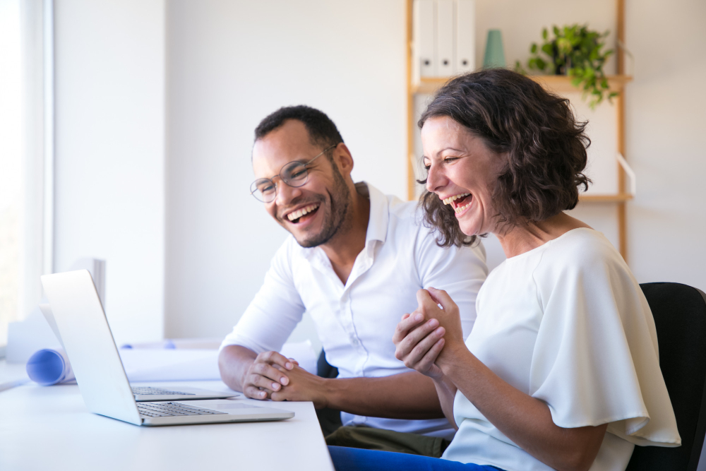 Two people smiling and looking at a laptop screen in an office setting