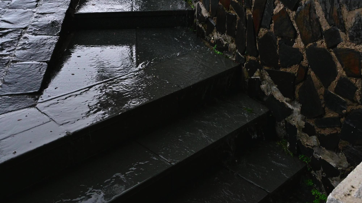 Wet stone steps with water flowing down next to a stone wall