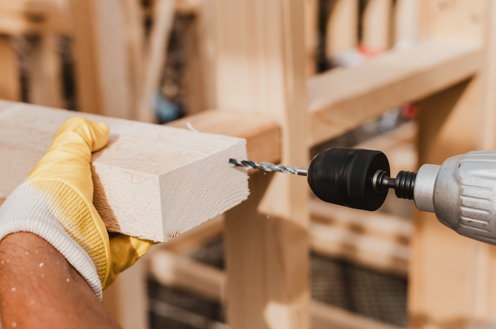Close-up of a person using a drill on a wooden plank.