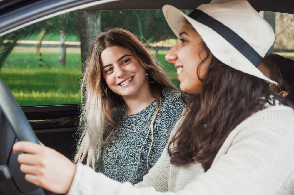 Two women sitting in a car, one driving and the other smiling at her.