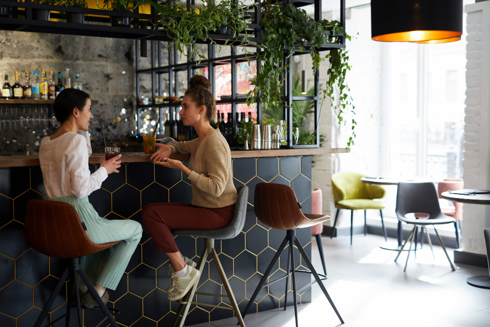 Two women sitting at a modern cafe bar with plants and geometric decor