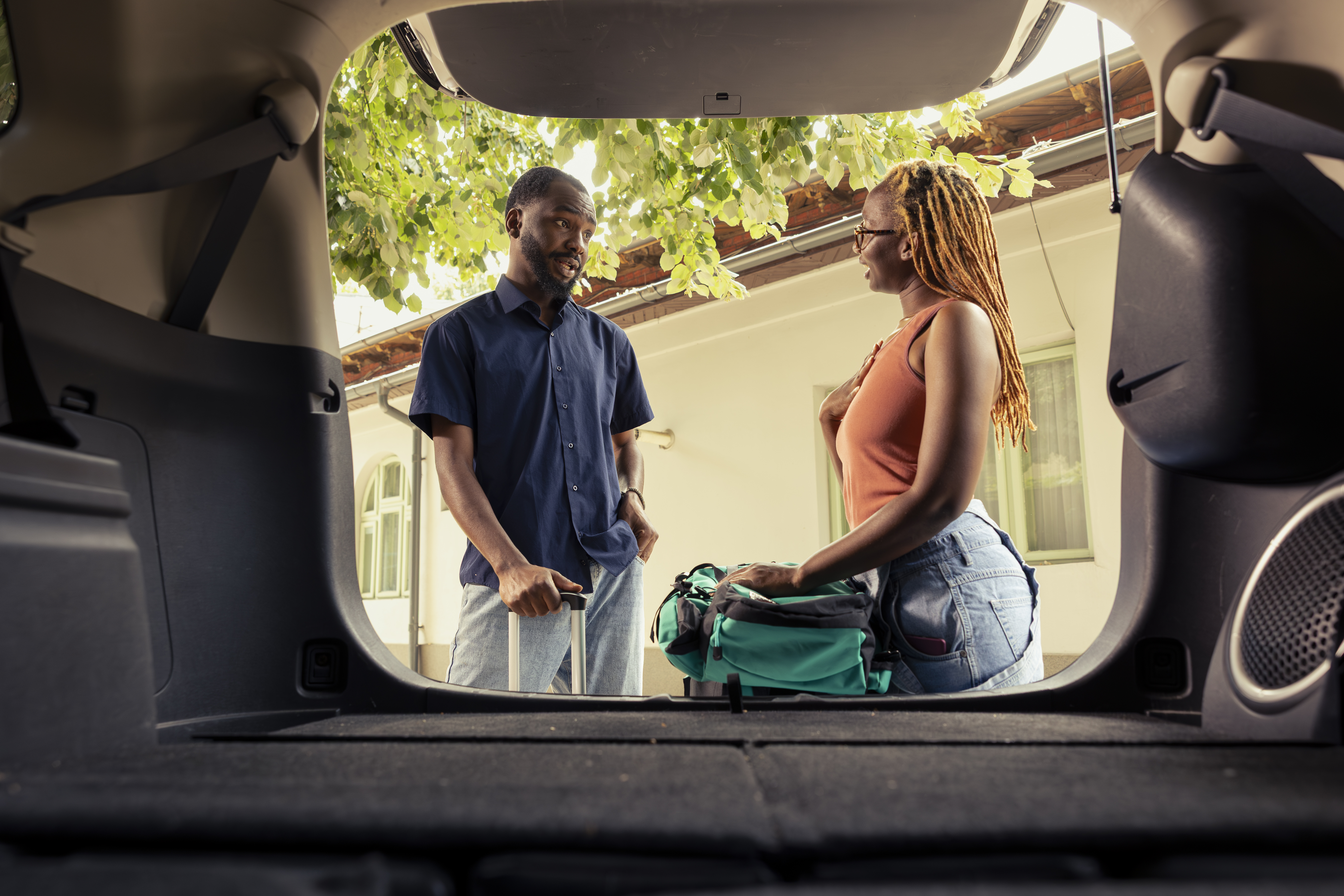 View from inside a car trunk showing a man and woman with luggage outside.