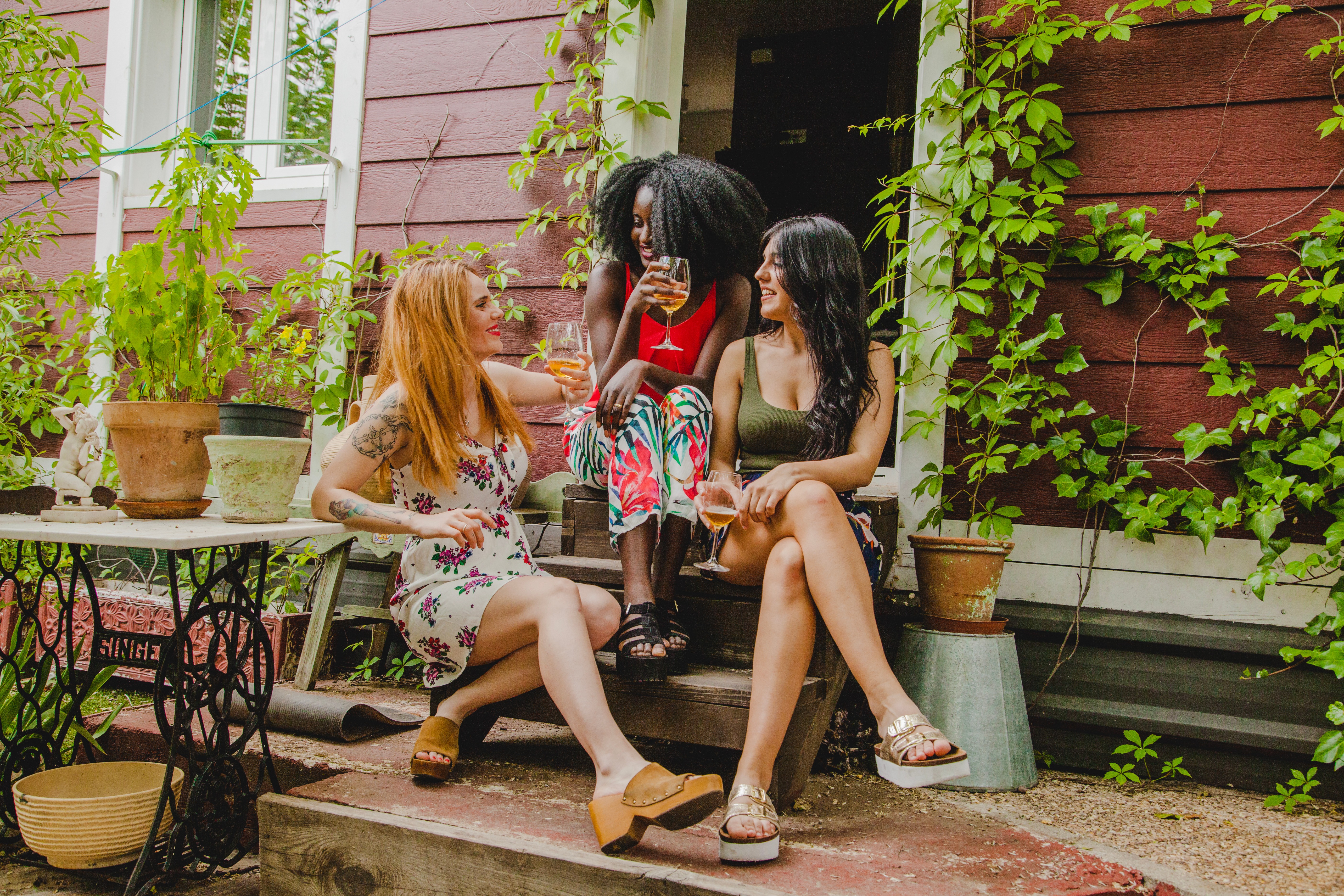 Three women sitting on porch steps enjoying drinks and conversation