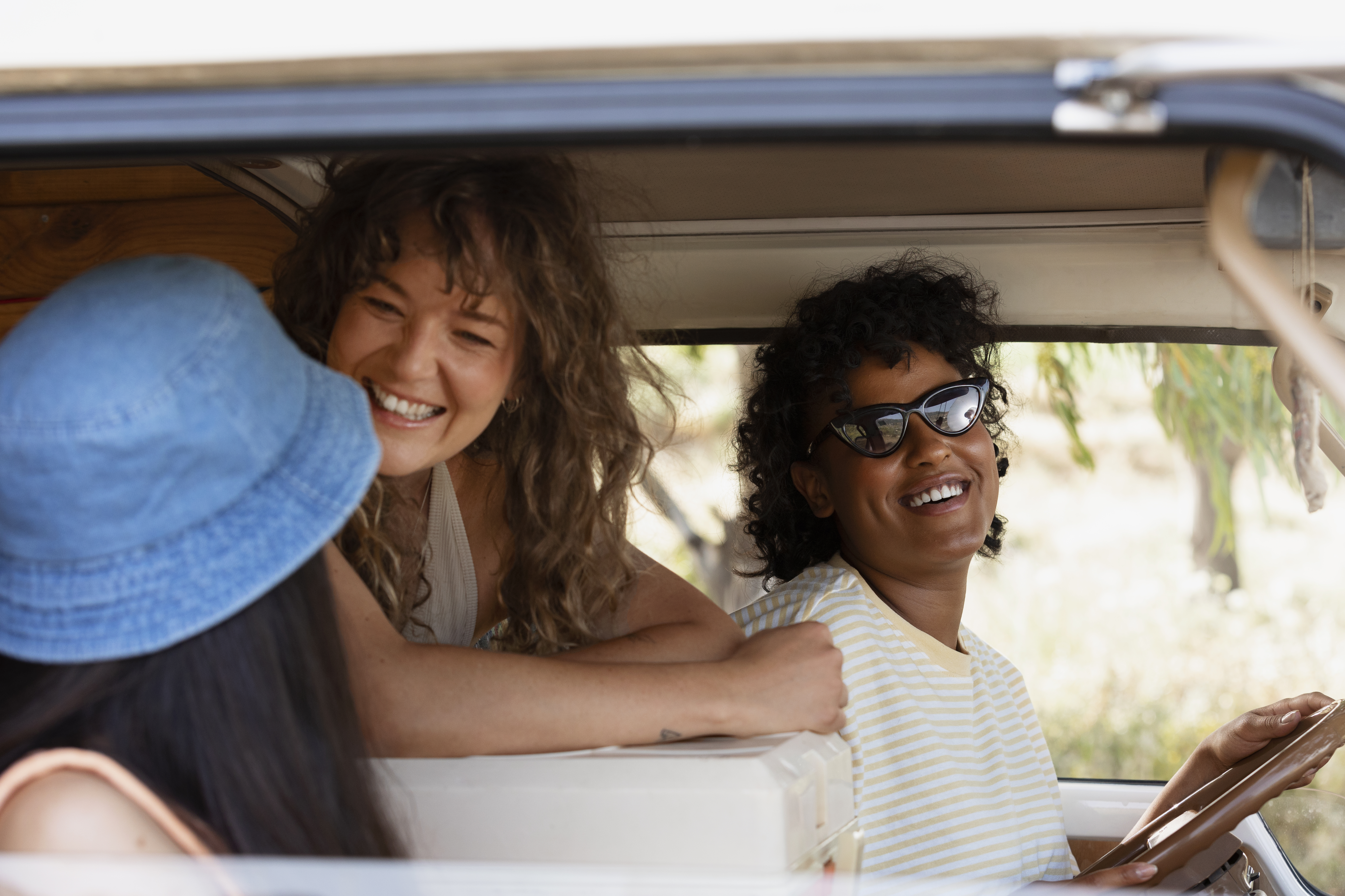 Three friends smiling and enjoying a road trip in a car.