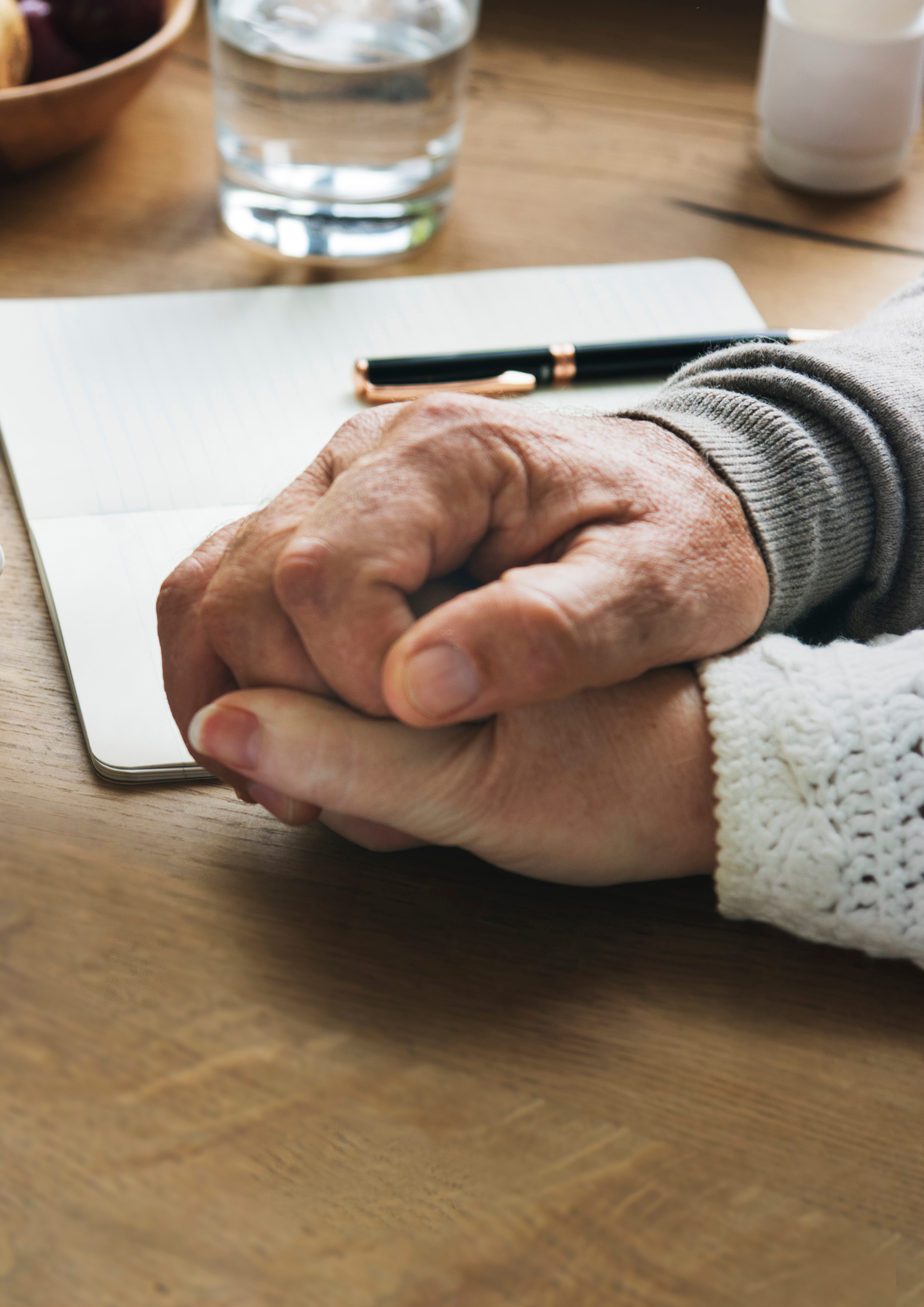 Close-up of two people holding hands on a wooden table with a notebook and pen nearby
