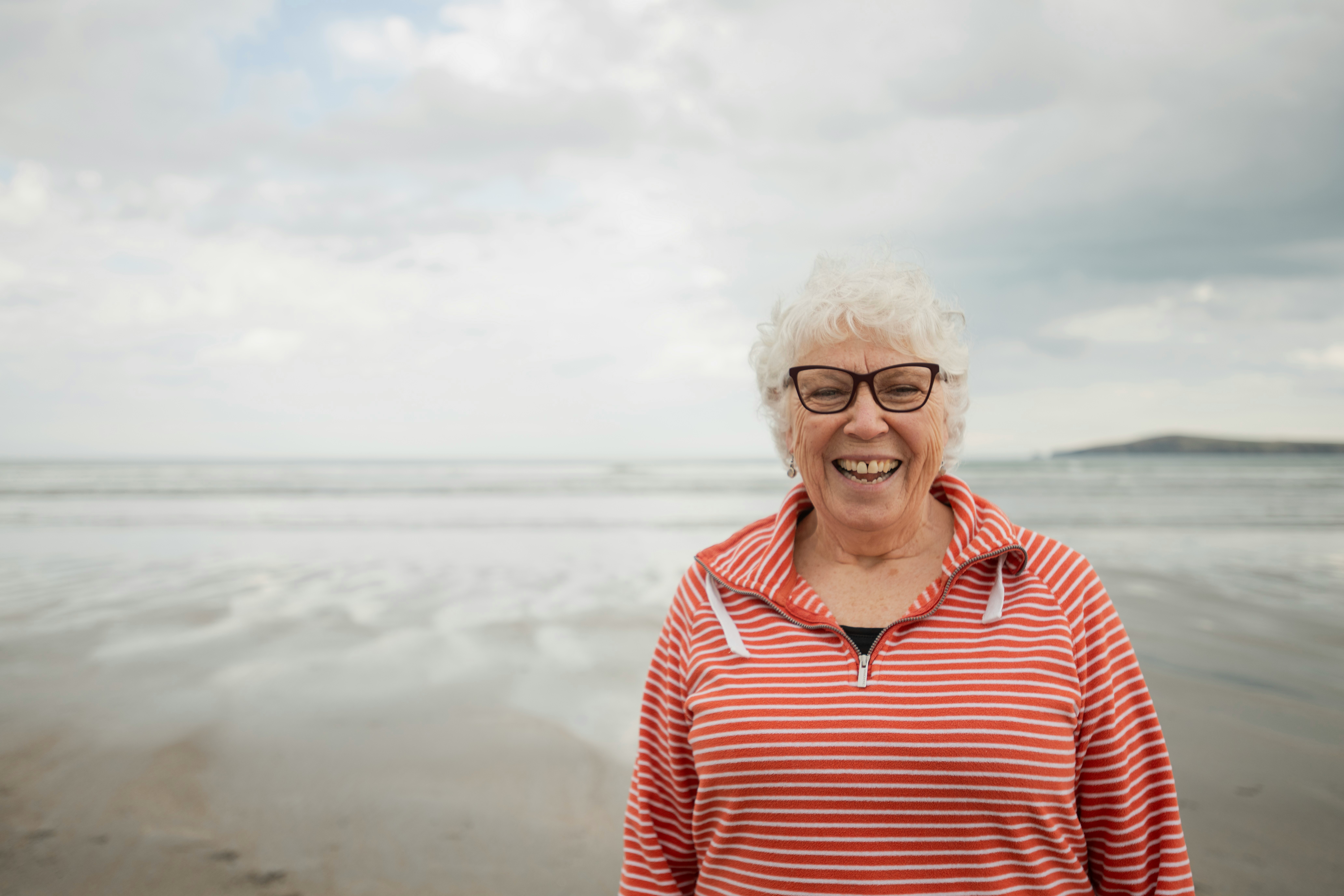 Smiling elderly woman in a striped sweater standing on a beach