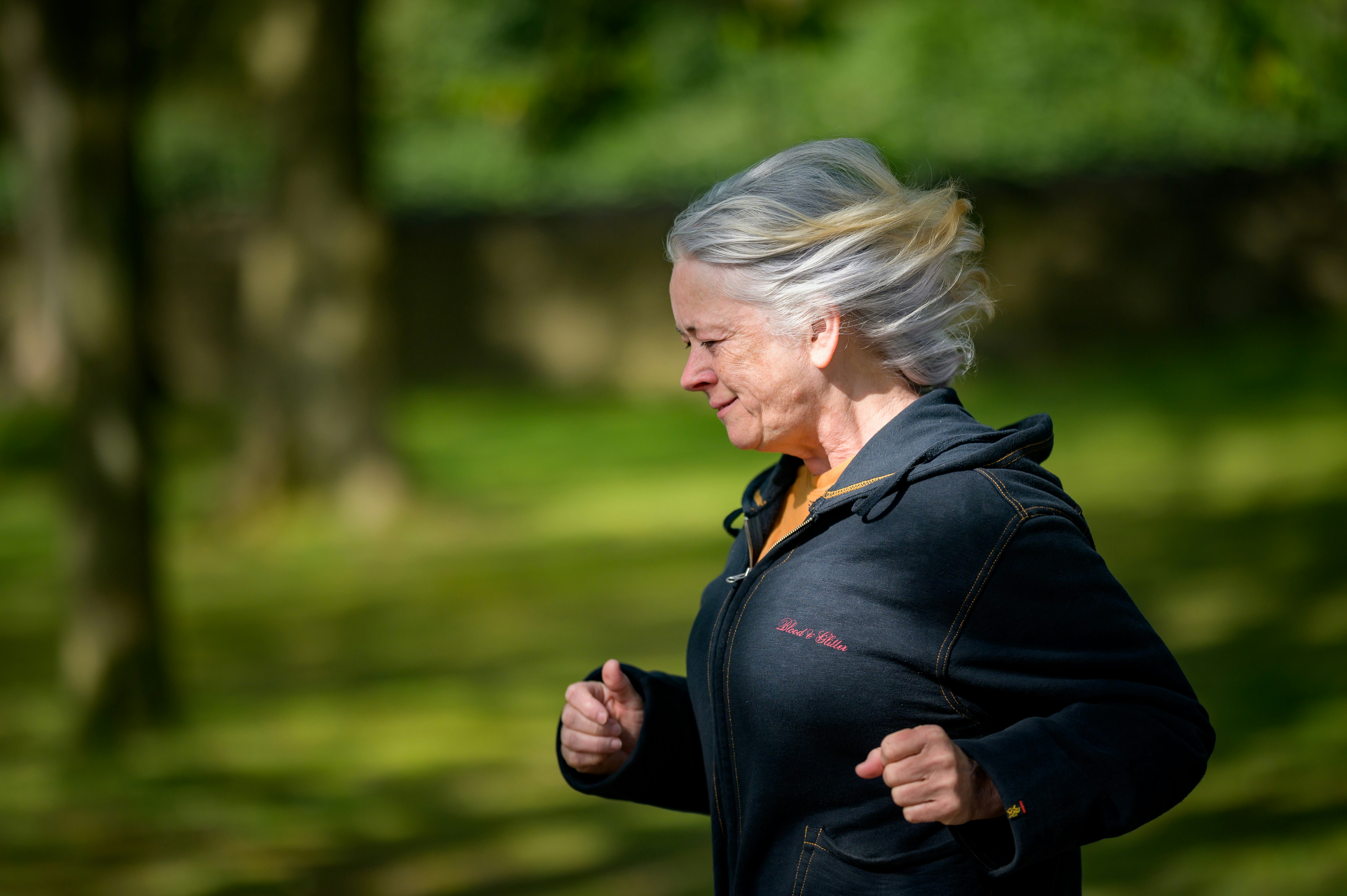 Older woman jogging in a park with trees in the background