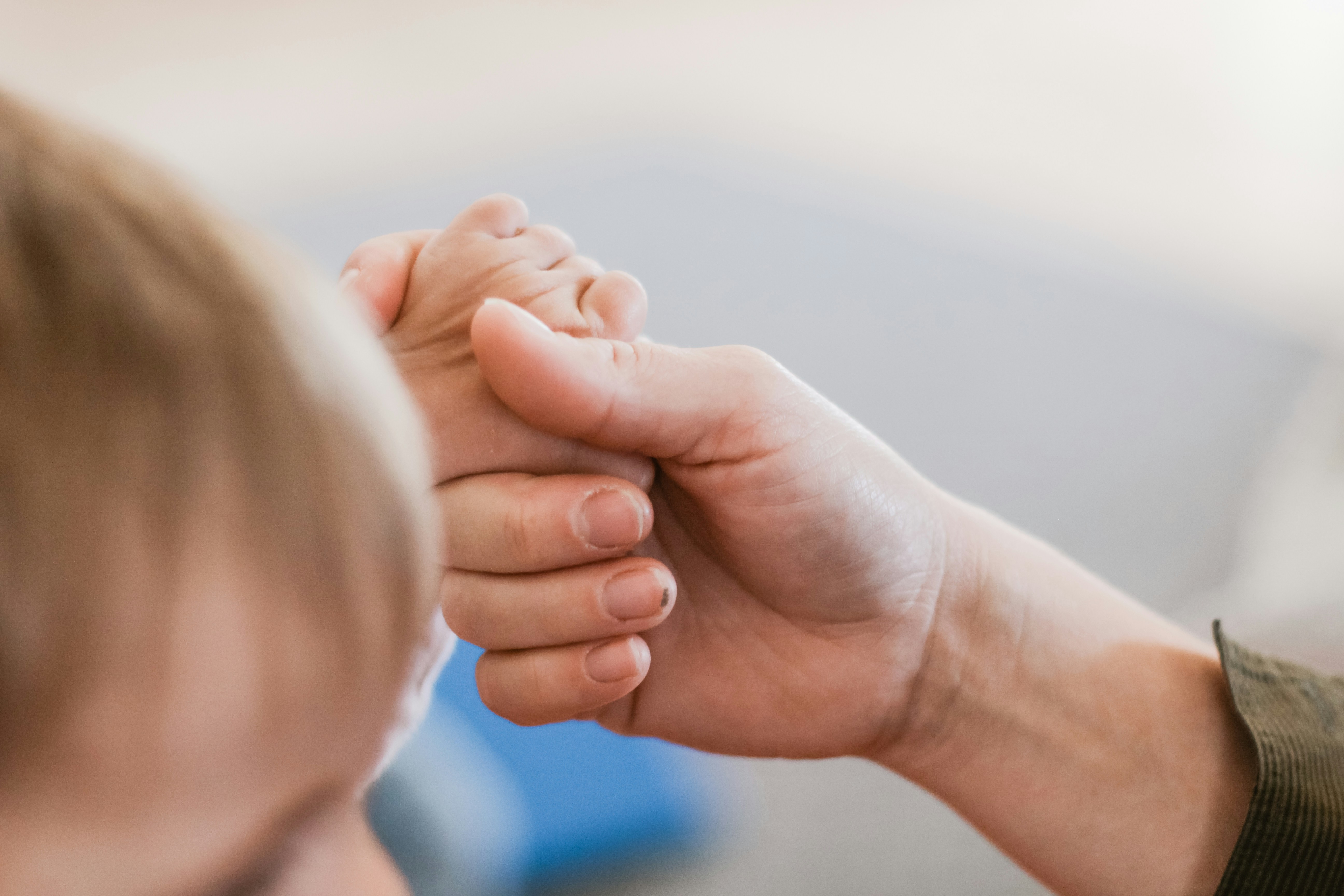 Close-up of an adult holding a child's hand gently
