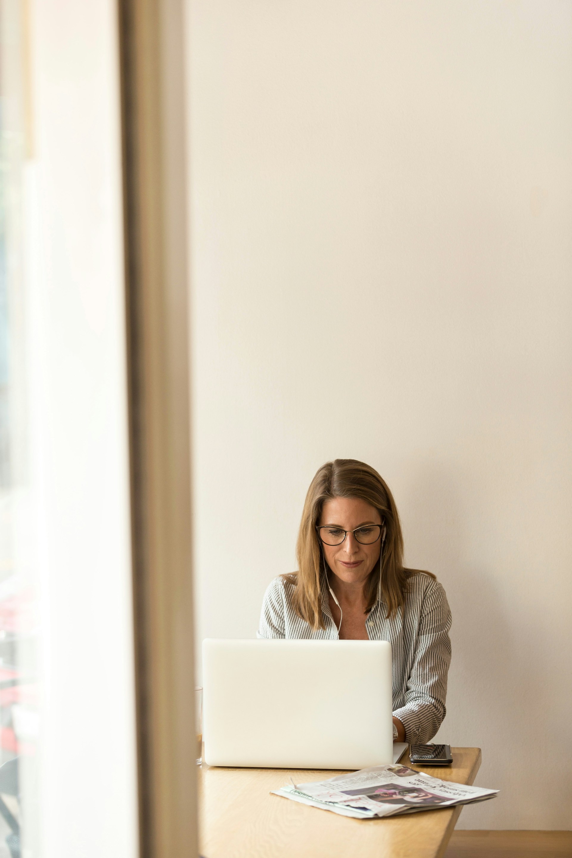 Woman working on a laptop at a wooden table with papers nearby