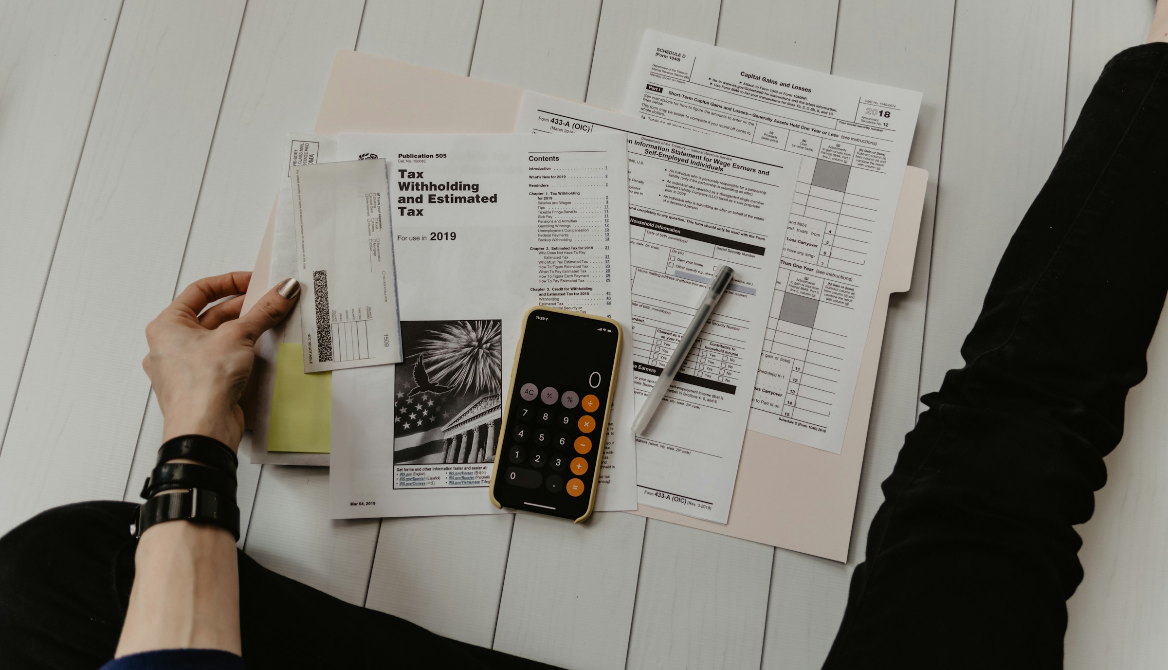 Person using a calculator with tax documents spread on the floor