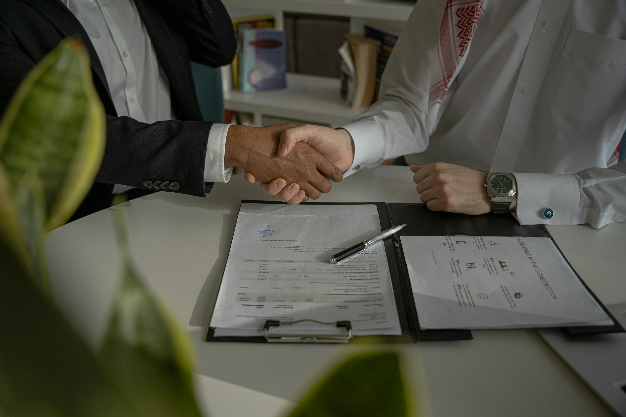 Two people shaking hands over a table with documents and a pen