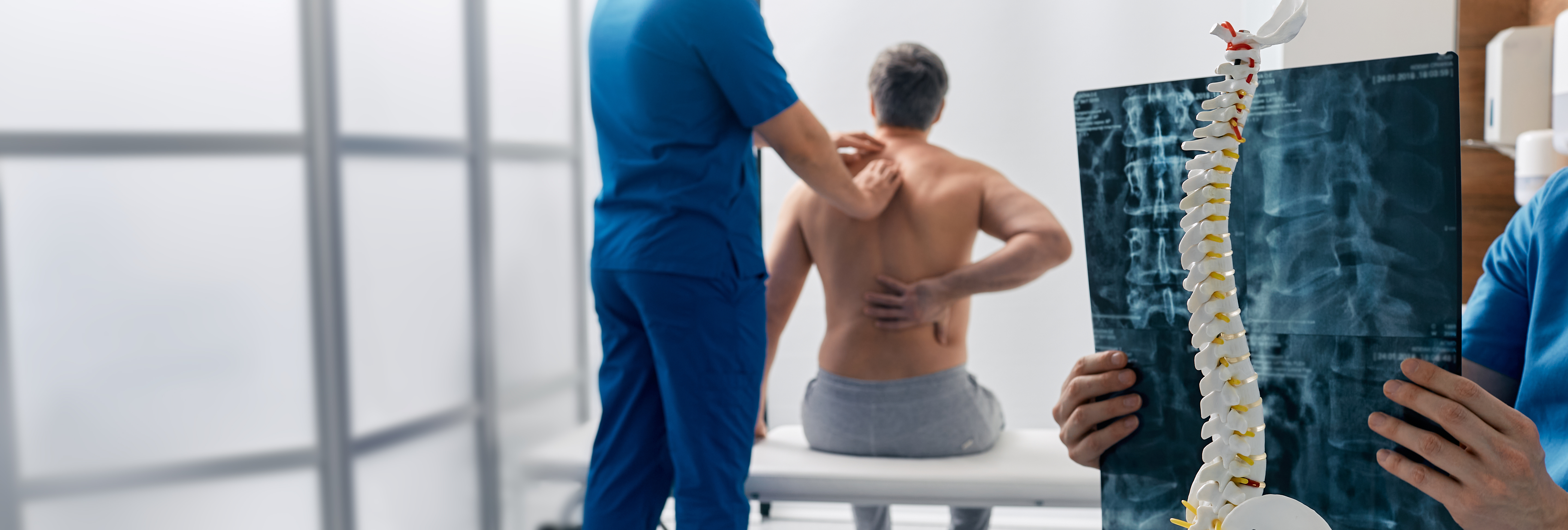 Physical therapist gently examining a patient’s neck and shoulder from behind