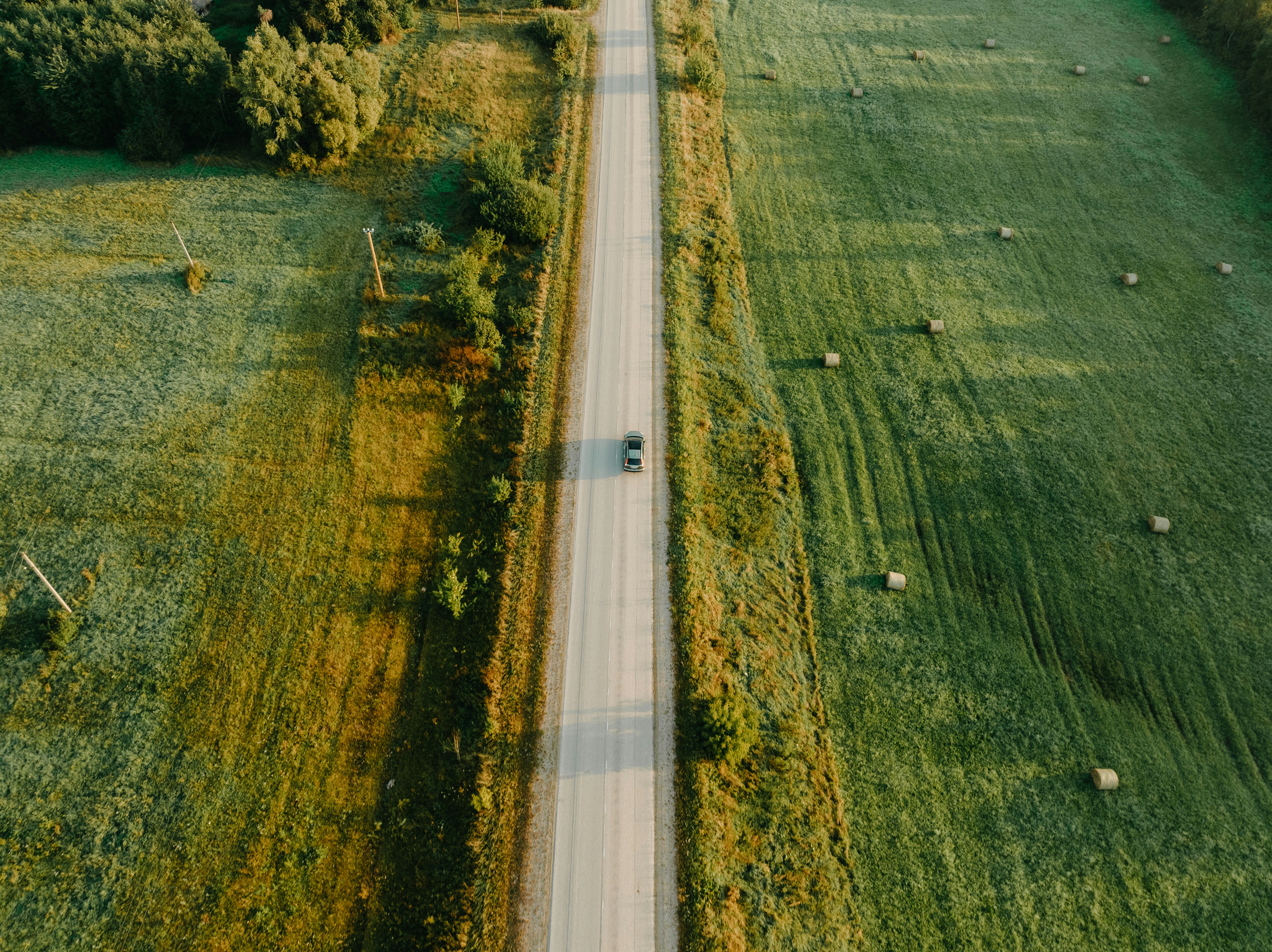 Aerial view of a car driving on a rural road between fields