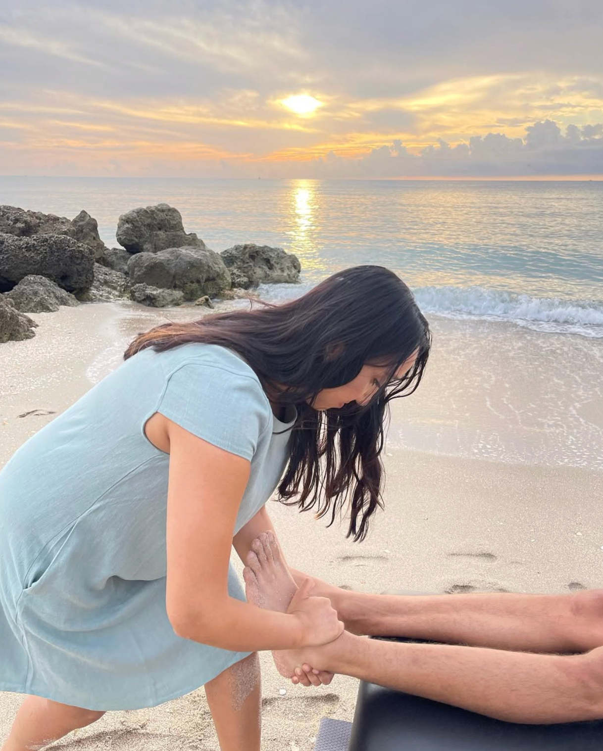 Therapist performing foot massage on a beach at sunset