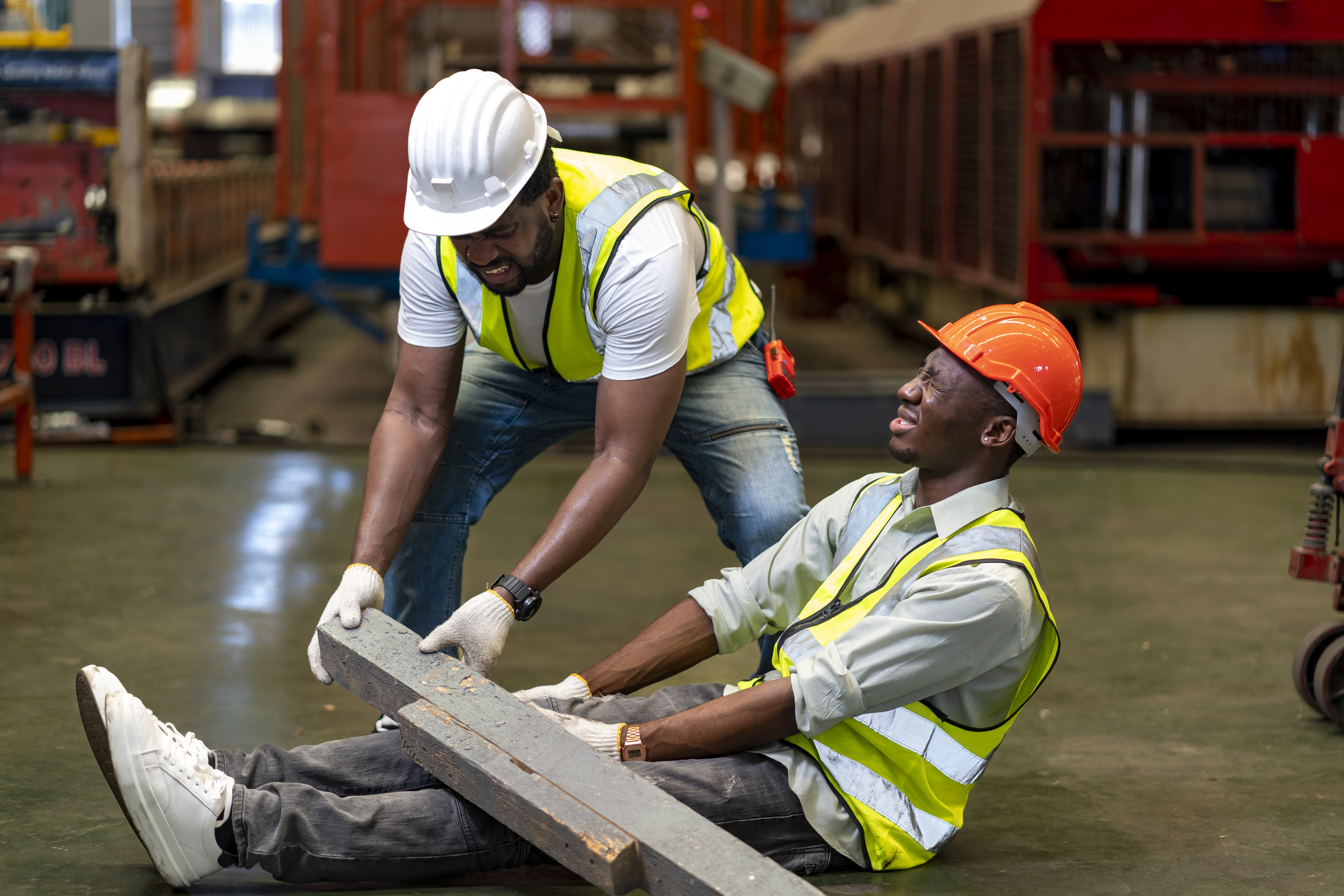 Worker in a hard hat assisting an injured colleague in a factory setting