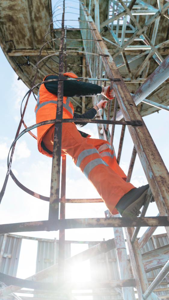 Construction worker in orange safety gear climbing a metal ladder.