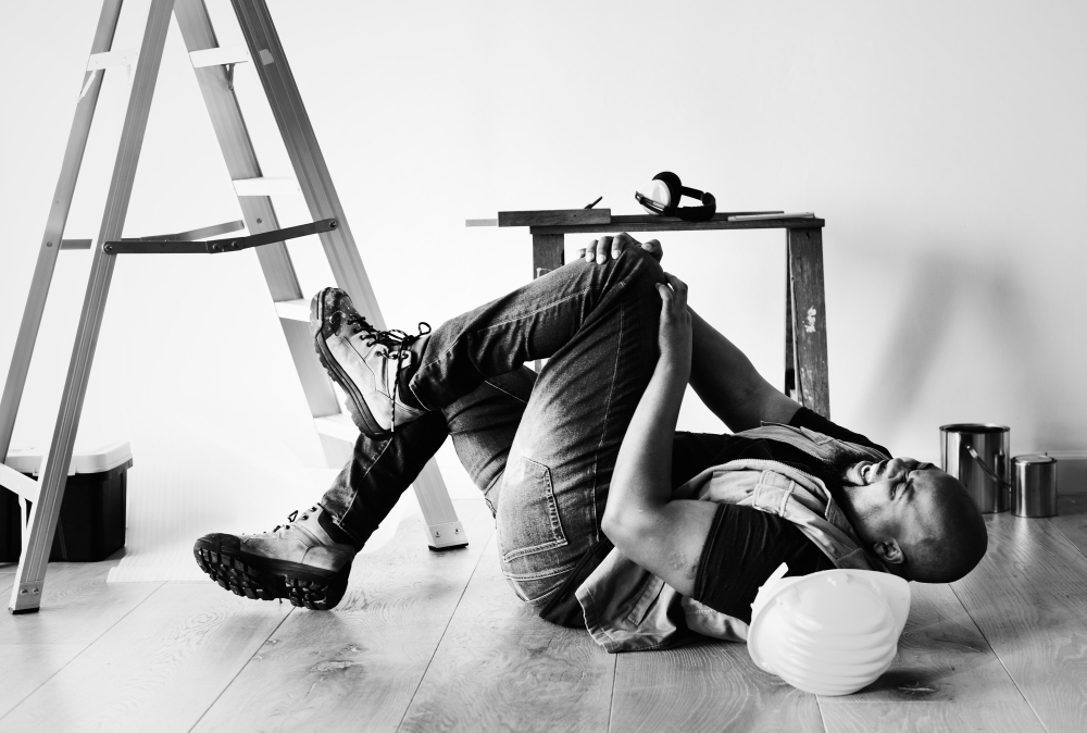 Construction worker lying on the floor in pain near a ladder.