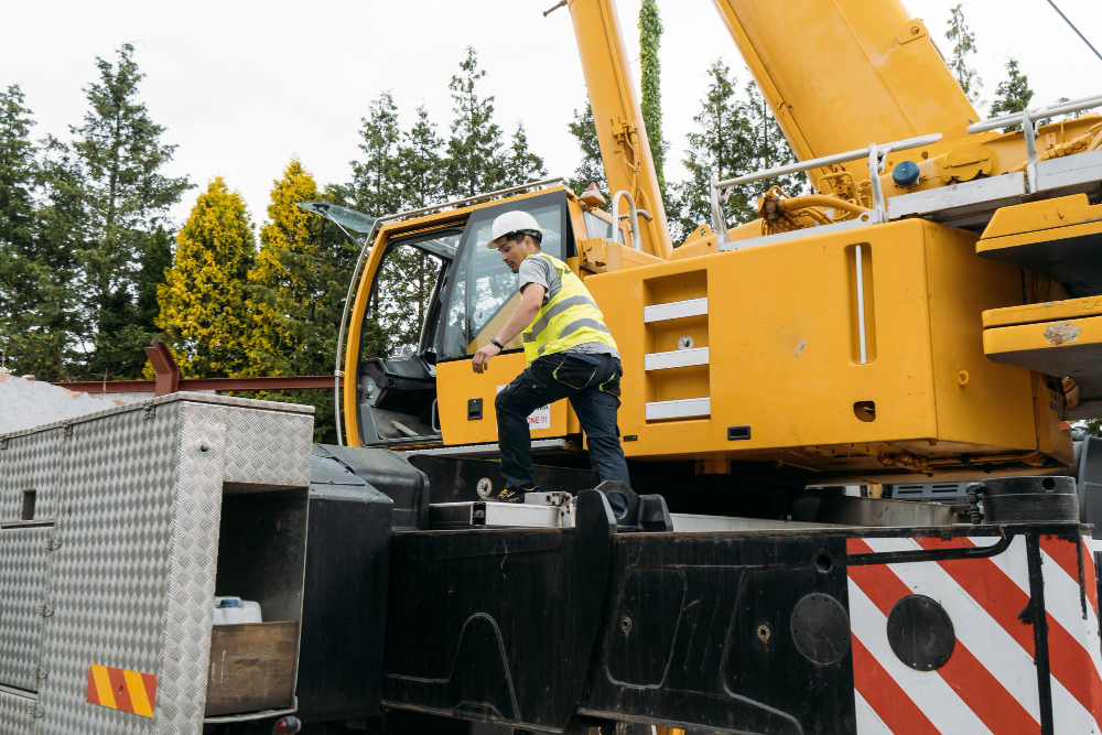 Construction worker climbing onto a yellow crane at a worksite.