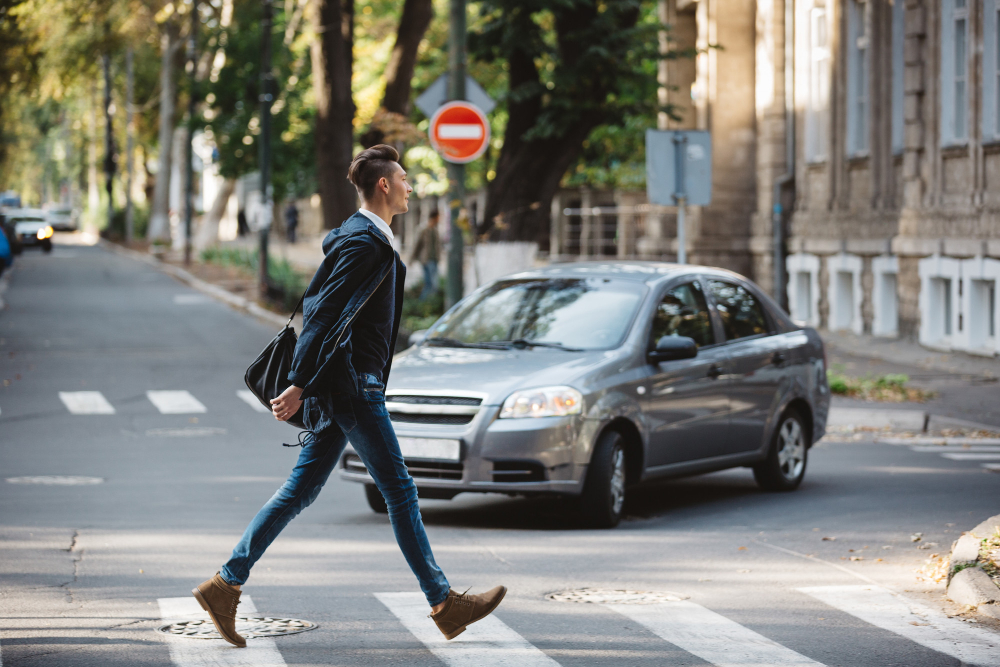 Man crossing the street at a crosswalk with a car approaching.