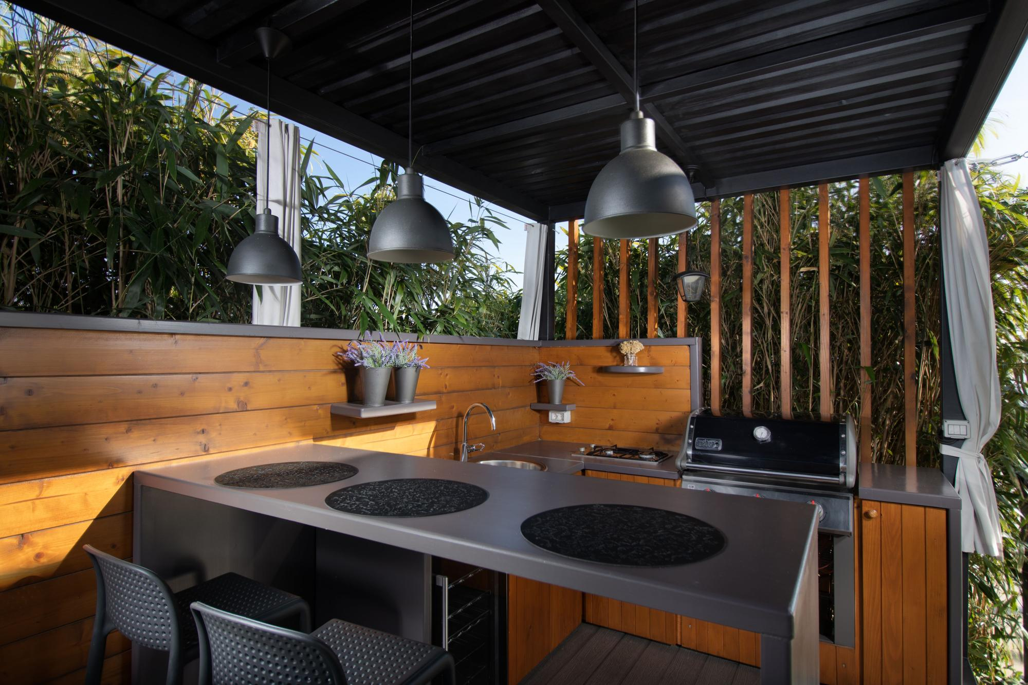 Outdoor kitchen with wooden paneling, pendant lights, and a grill