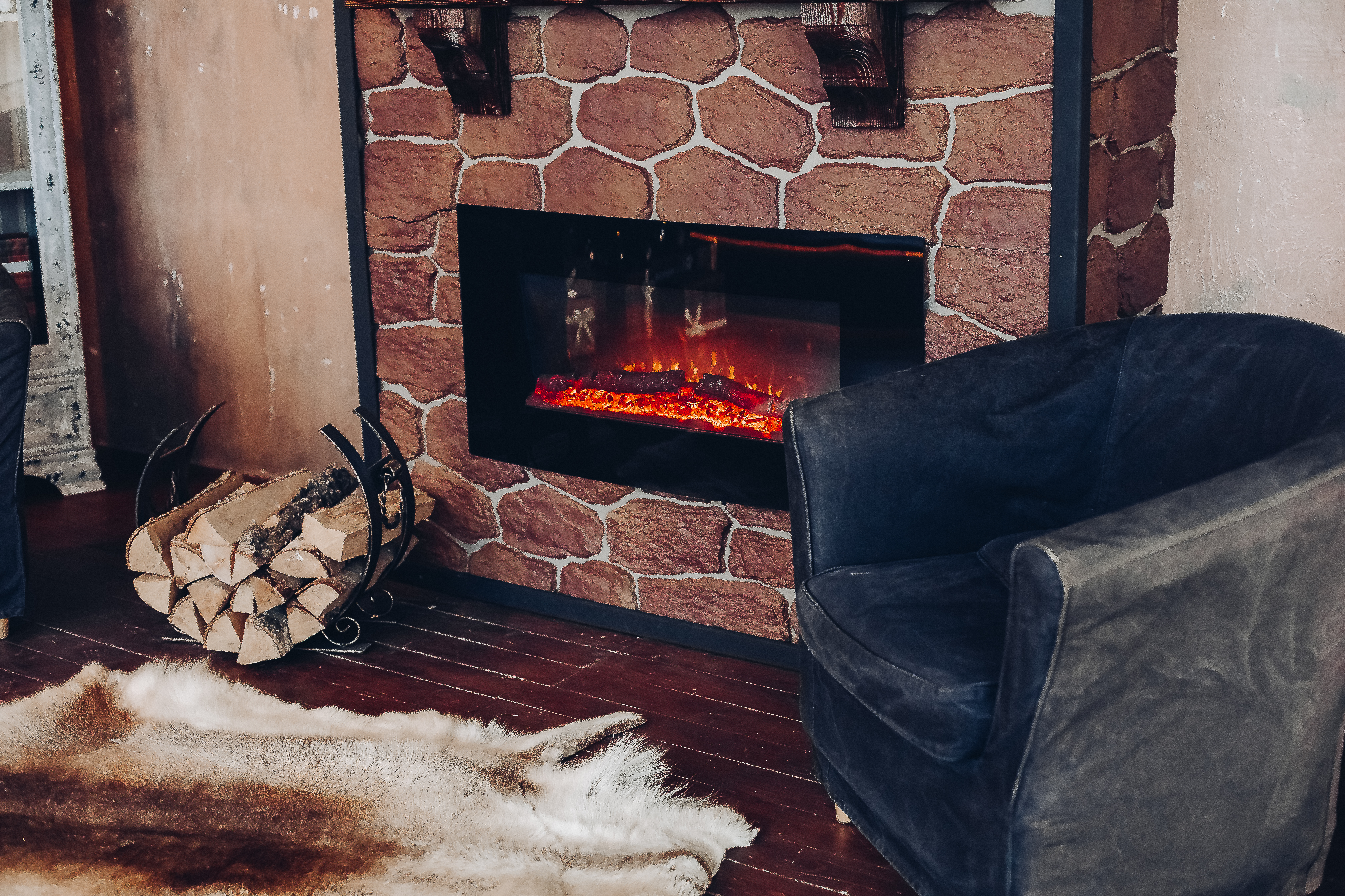 Cozy living room with a stone fireplace, armchair, and firewood.