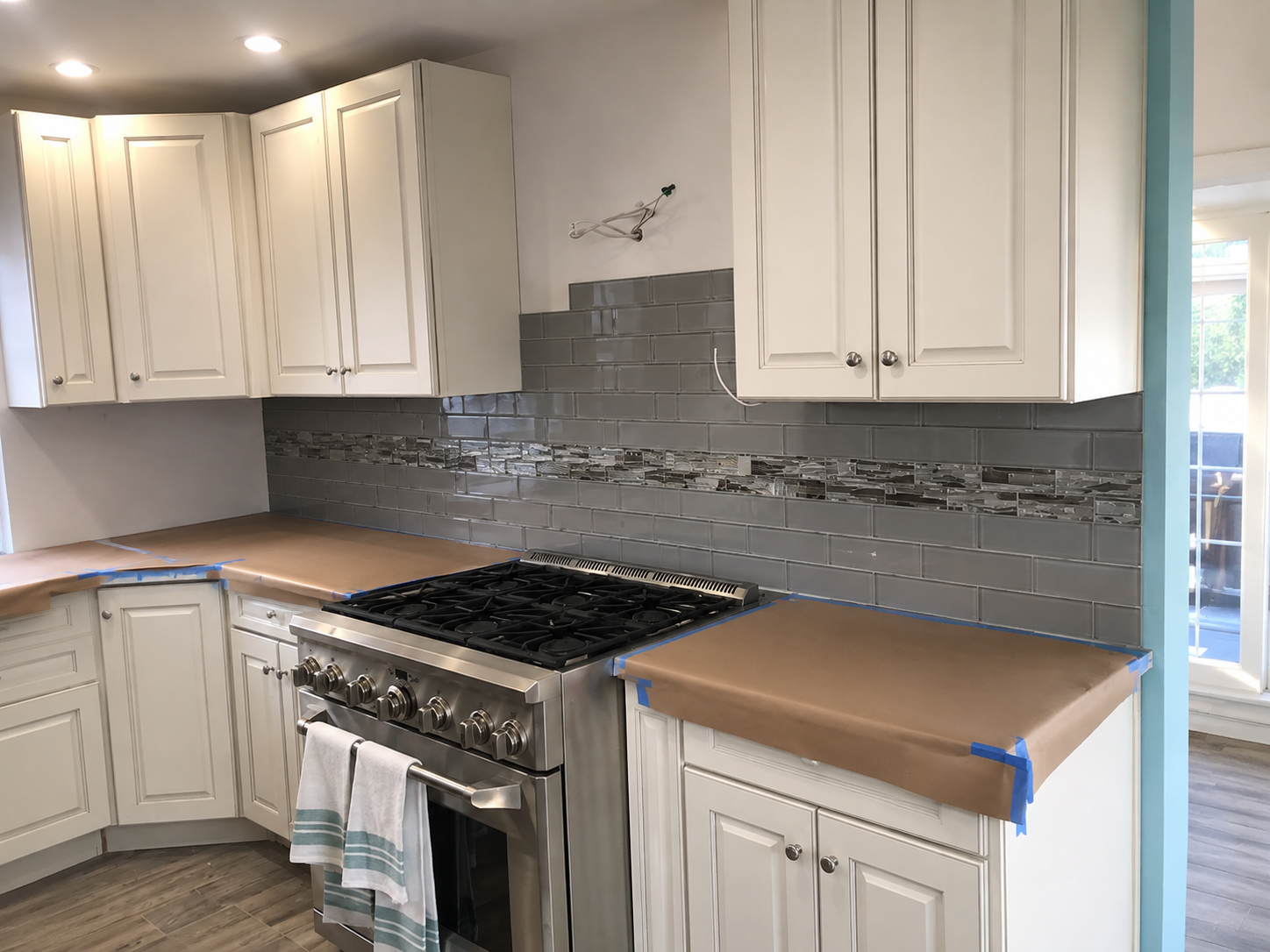 Modern kitchen with white cabinets, stainless steel stove, and gray tile backsplash.