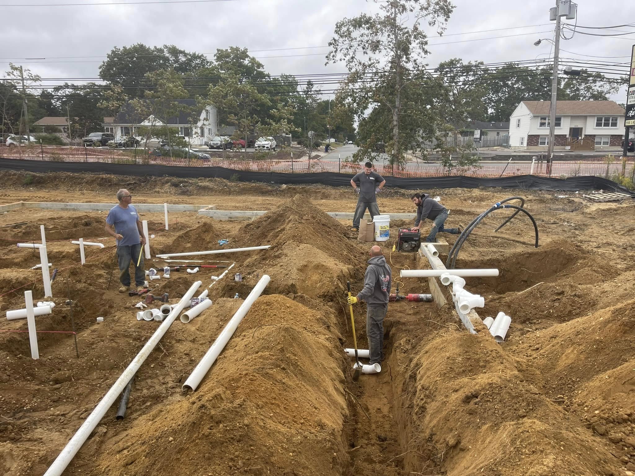 Construction workers installing plumbing pipes in a trench at a construction site.
